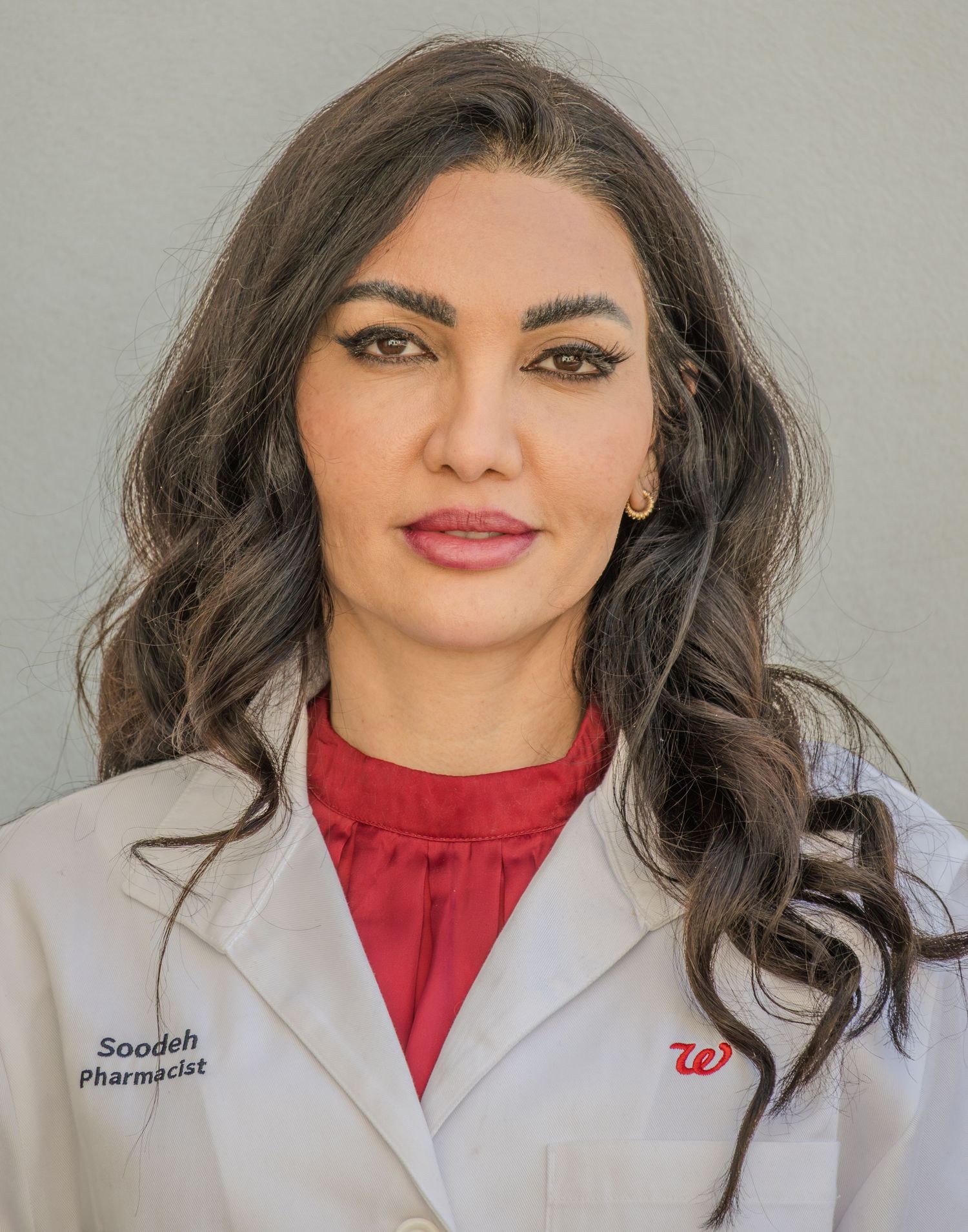 Healthcare professional in white lab coat and red blouse smiles warmly in professional headshot portrait.