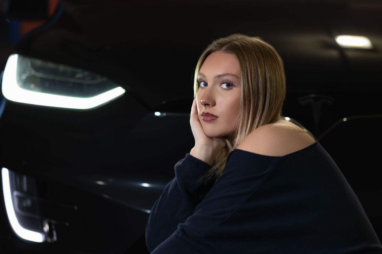 A woman in a dark interior looks out through a car window with dramatic lighting and reflections.