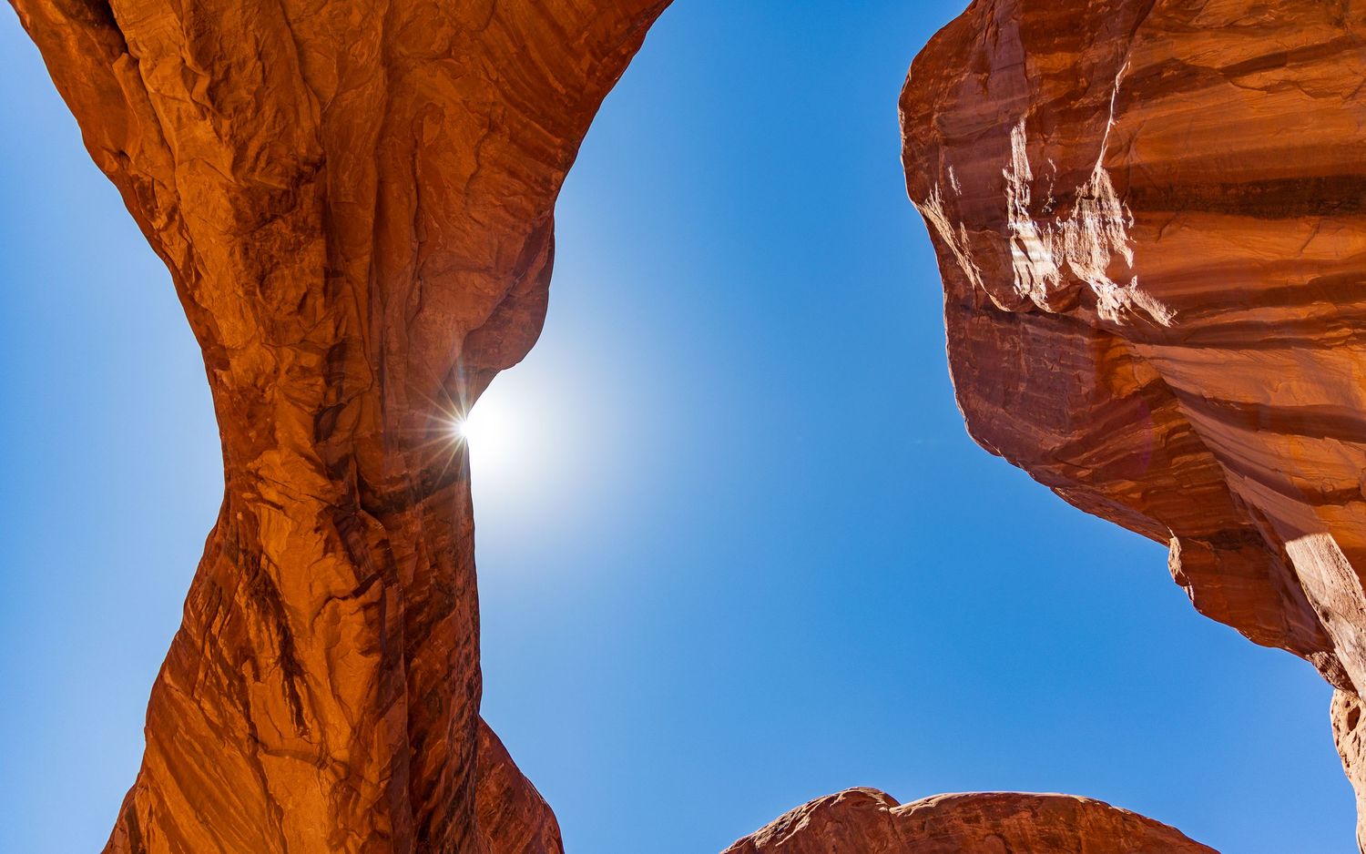 Natural stone arch formation in Arches National Park framing bright sunlight against blue sky.