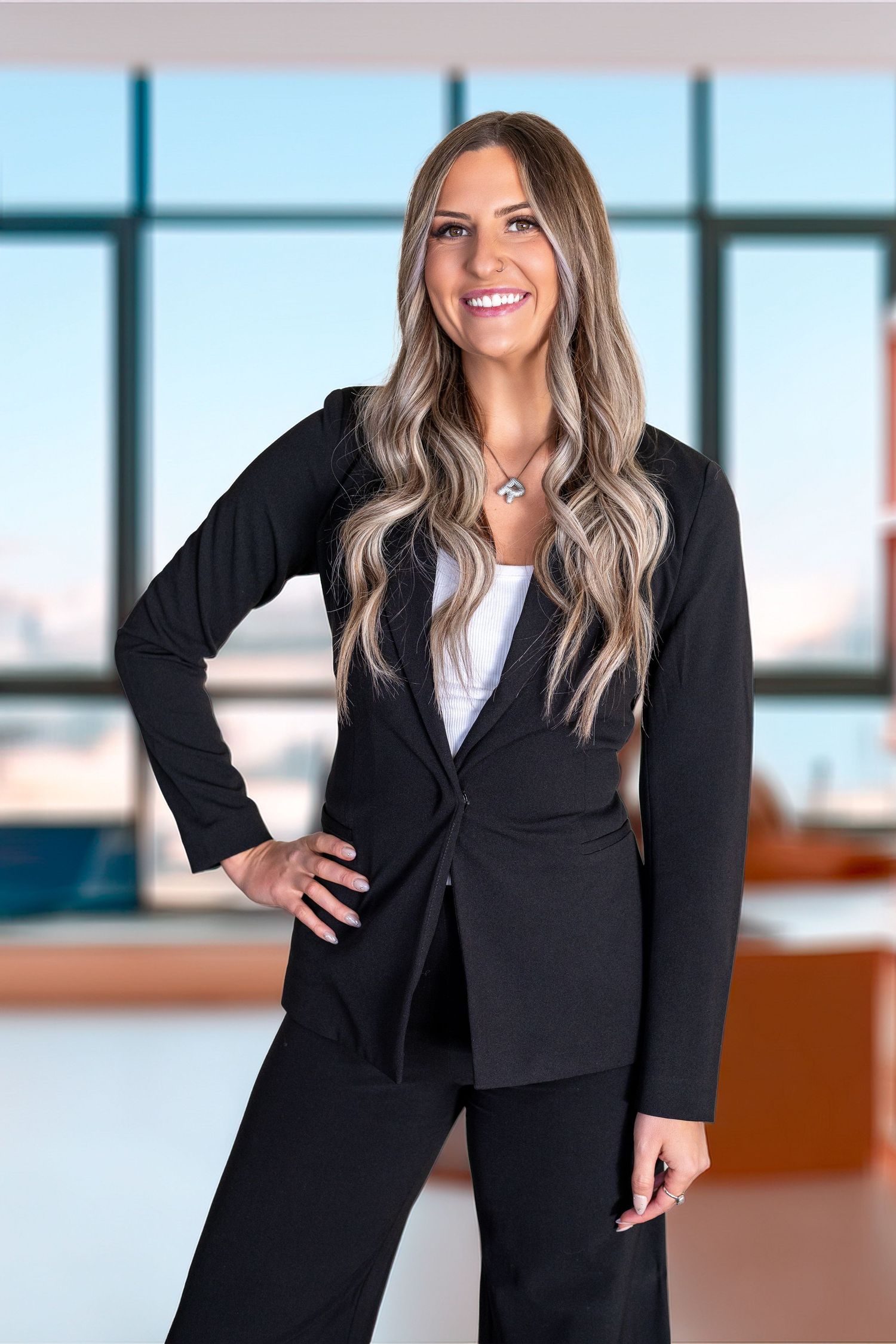Professional woman in black suit with long blonde hair smiling confidently in a modern office setting.
