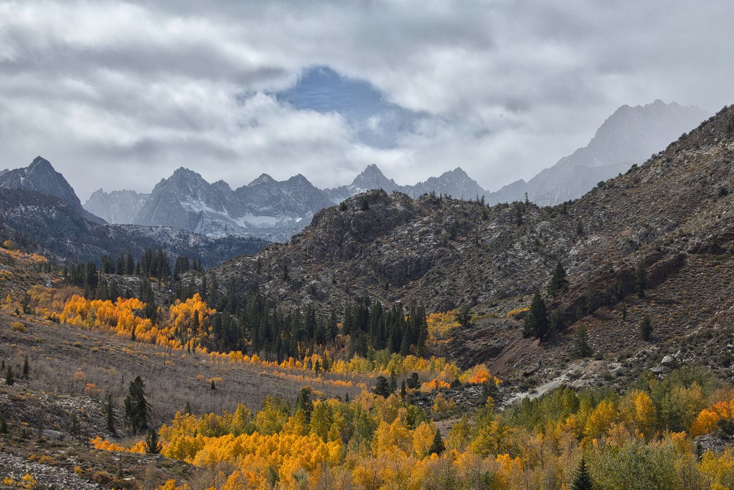 Scenic mountain landscape with golden aspen trees and dramatic cloudy skies in autumn.