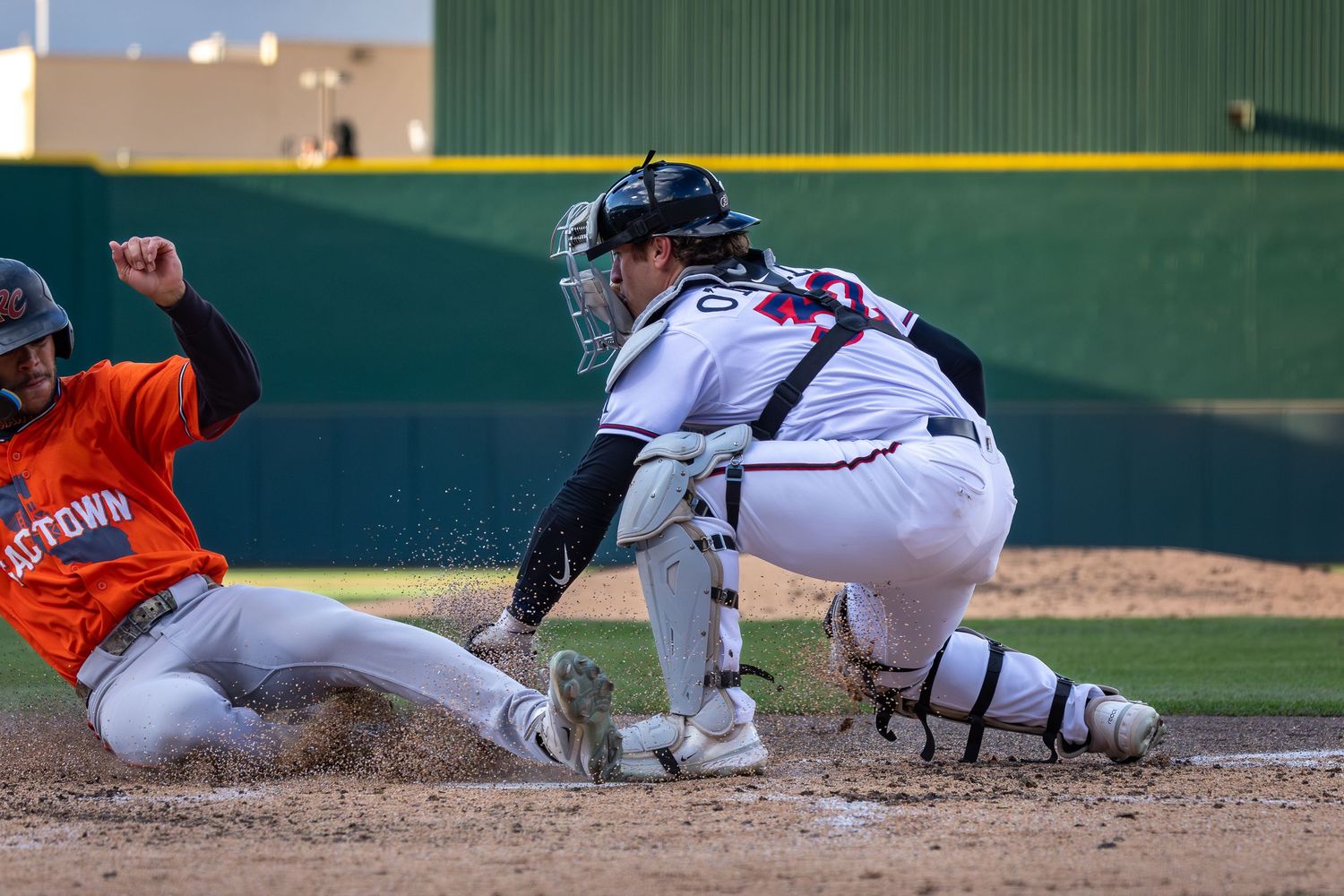 Baseball player sliding into home plate as catcher attempts tag during competitive game.