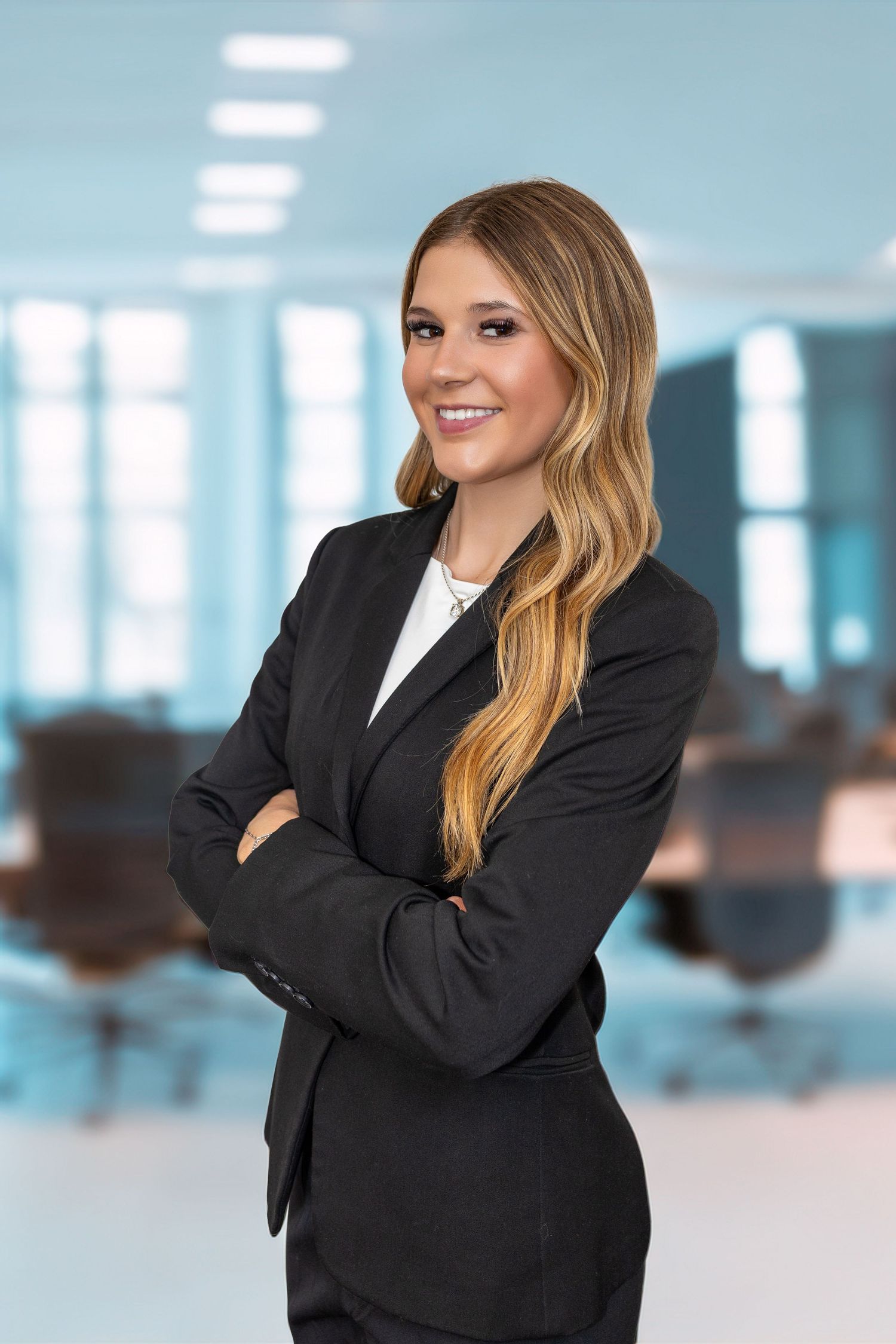 Smiling businesswoman in black suit with arms crossed standing in modern office environment.