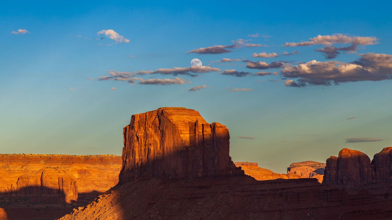Majestic sandstone butte in Monument Valley glowing orange at sunset against blue sky.