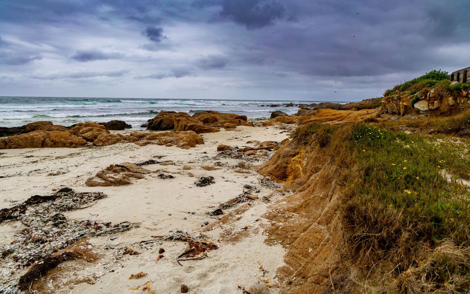Rocky coastal beach landscape with dramatic cloudy sky and rough waters.