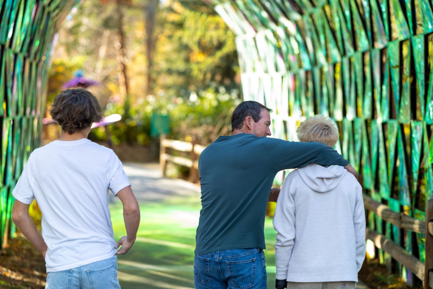 People walking on a green outdoor path surrounded by bamboo trees and natural lighting.