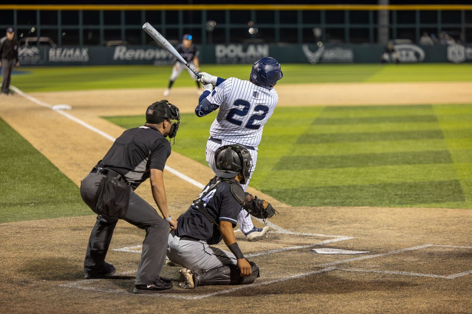 Baseball player #22 swings at pitch with catcher and umpire at home plate during a night game.