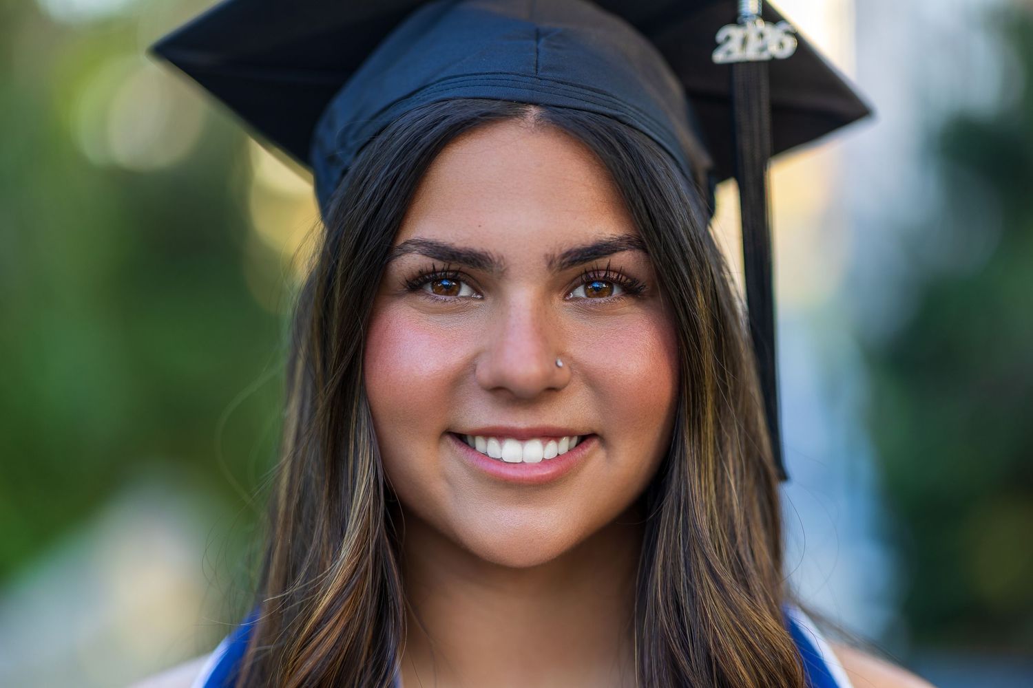 Smiling young woman in graduation cap and gown celebrating her academic achievement outdoors.