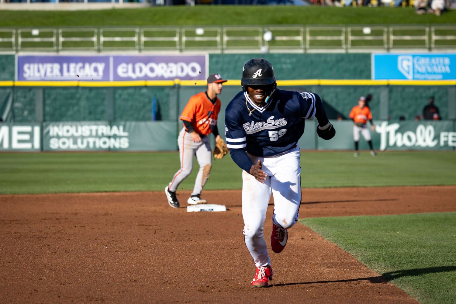 Baseball player in navy uniform rounds third base during a game at a stadium with Silver Legacy and Eldorado ads.
