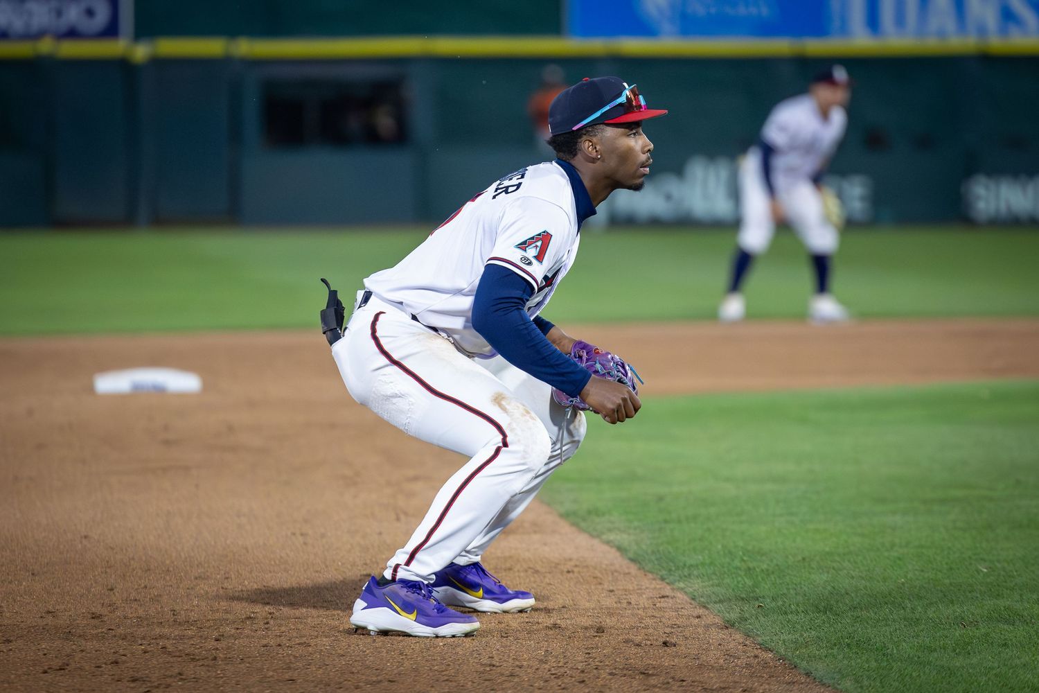 Baseball infielder in white Angels uniform crouches in ready position on the field during a night game.