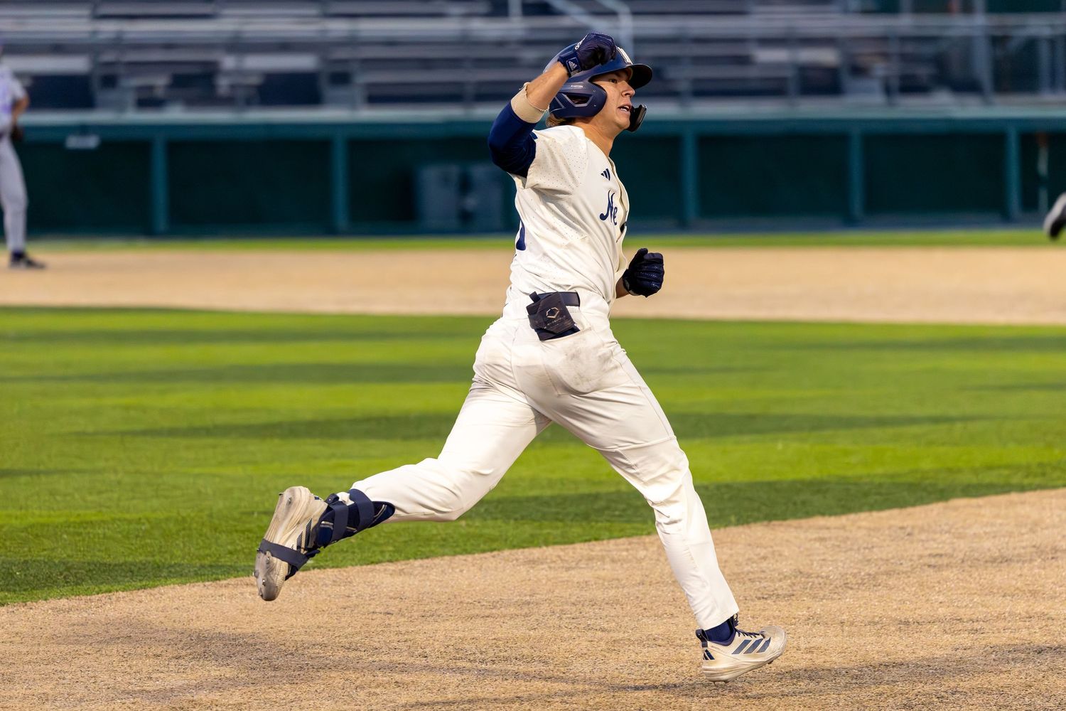 Baseball player in white uniform sprinting the bases during a night game under stadium lights.