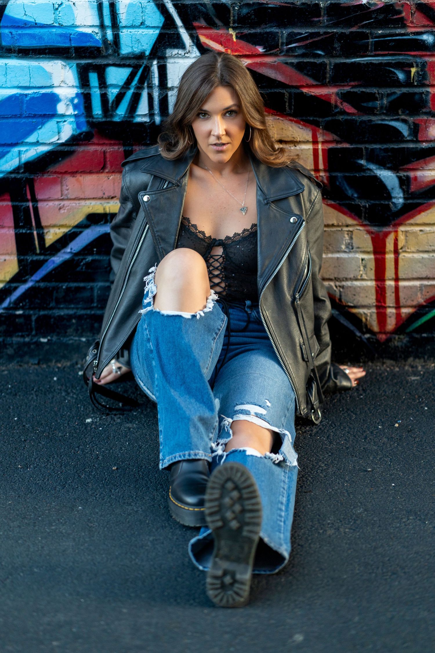 A fashion photo series showing edgy street style with ripped jeans, leather jacket and boots against a graffiti wall.