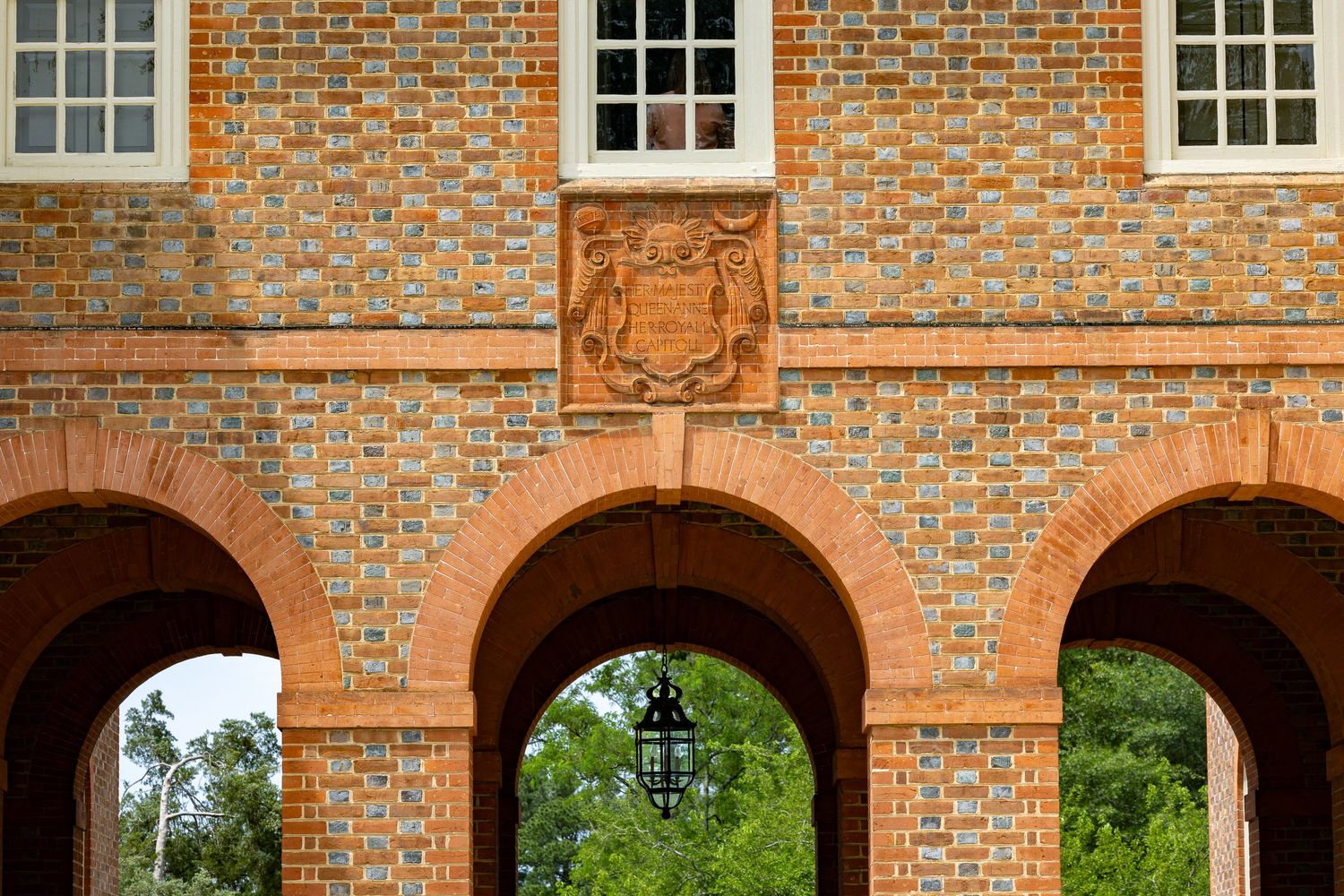 Historic brick building with ornate arched entryways, decorative coat of arms, and hanging lantern at a university campus.