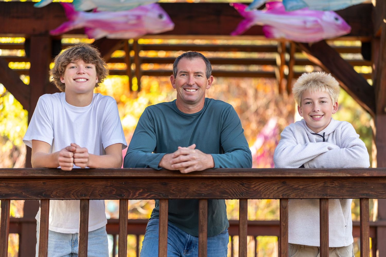 A group of people smile and pose together on a wooden deck with warm lighting in the background.