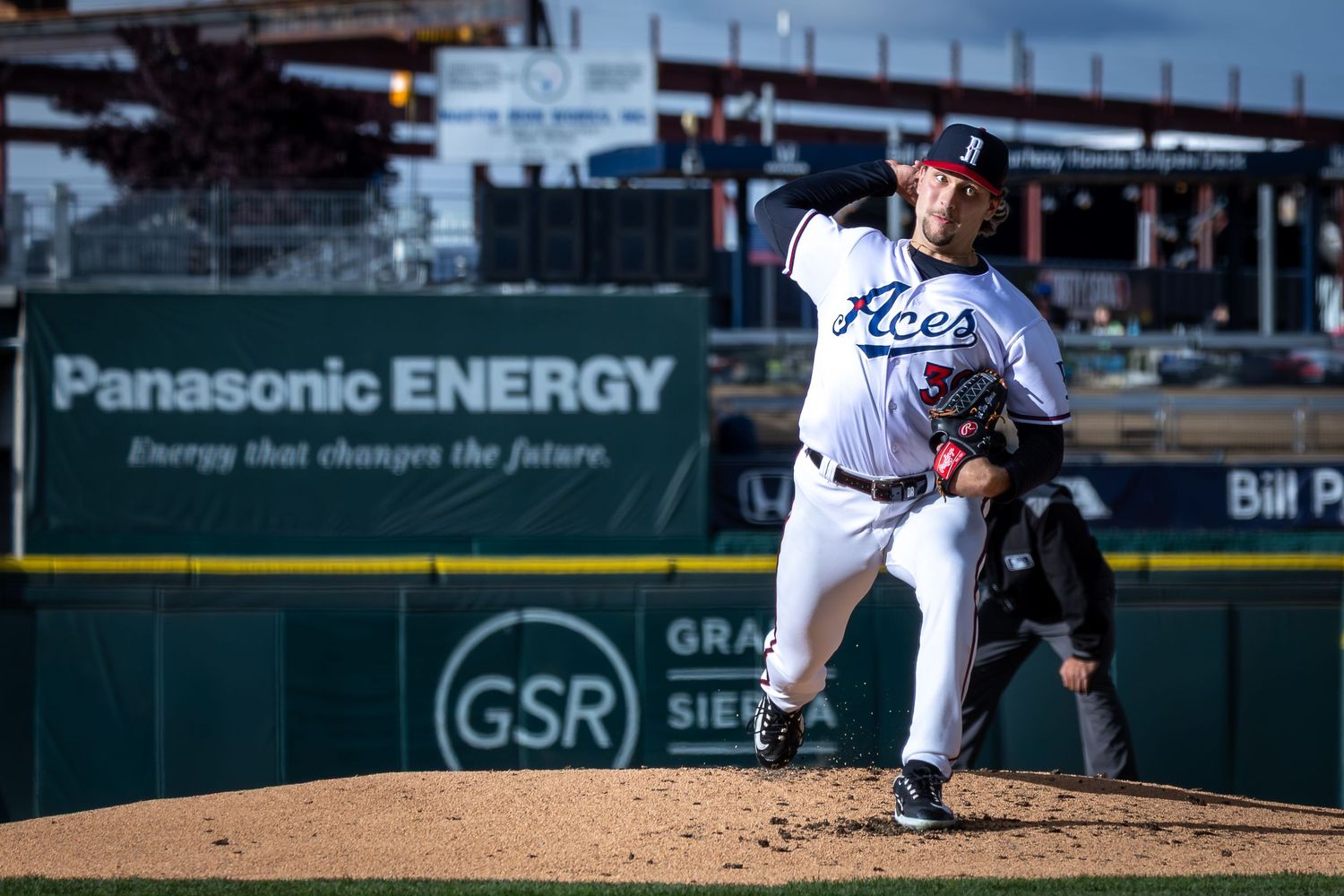 Baseball pitcher in Aces uniform winds up for a pitch at a professional stadium with Panasonic Energy signage.