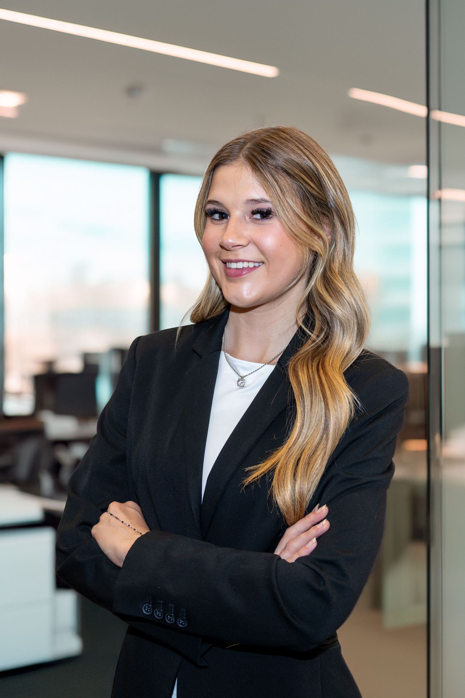 Young professional woman in black blazer smiling with arms crossed in modern office.