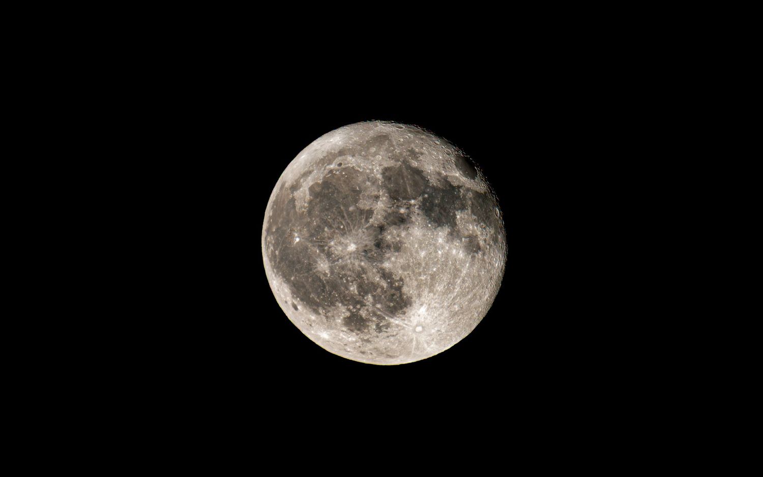 Full moon glows bright and detailed against black night sky.