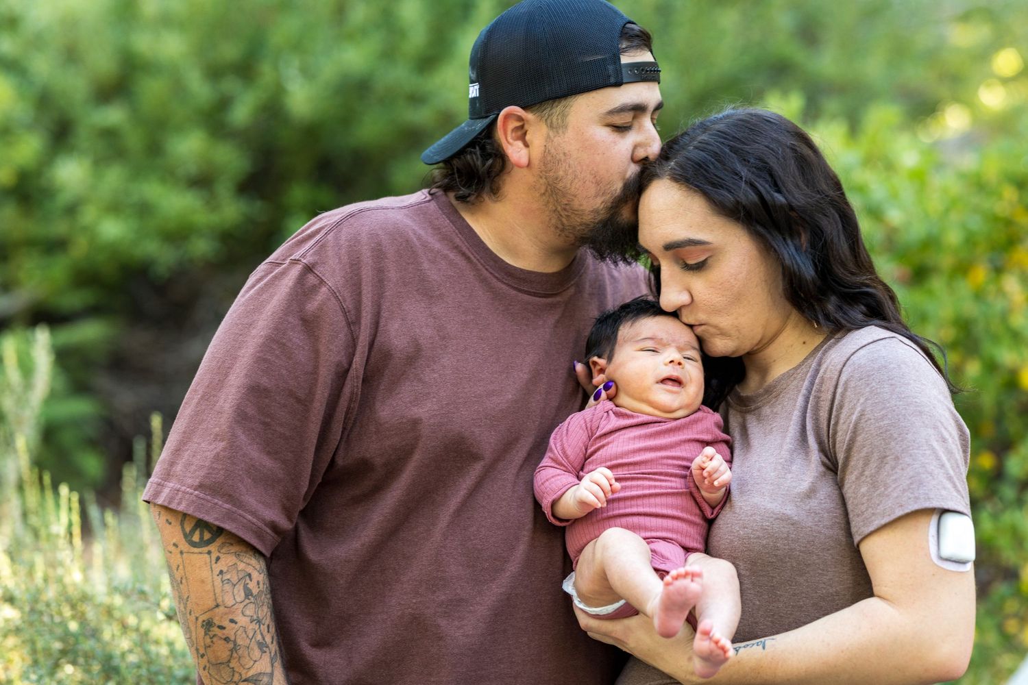 A happy family enjoys tender moments together outdoors in a lush green garden setting.