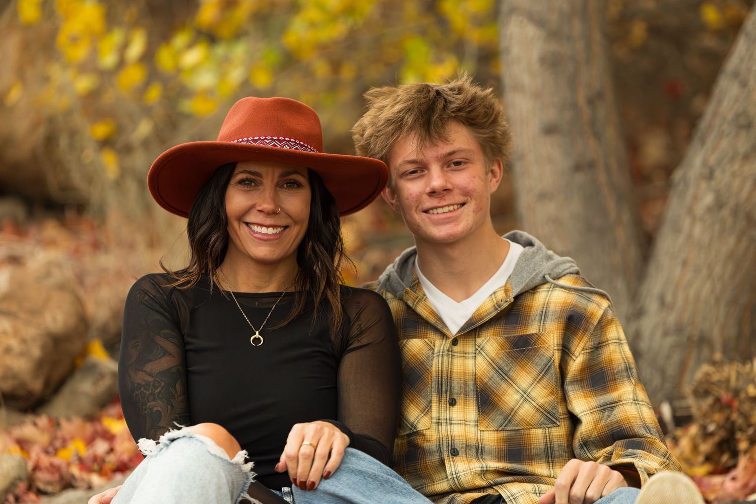 A couple poses together outdoors during autumn with colorful fall foliage in the background.