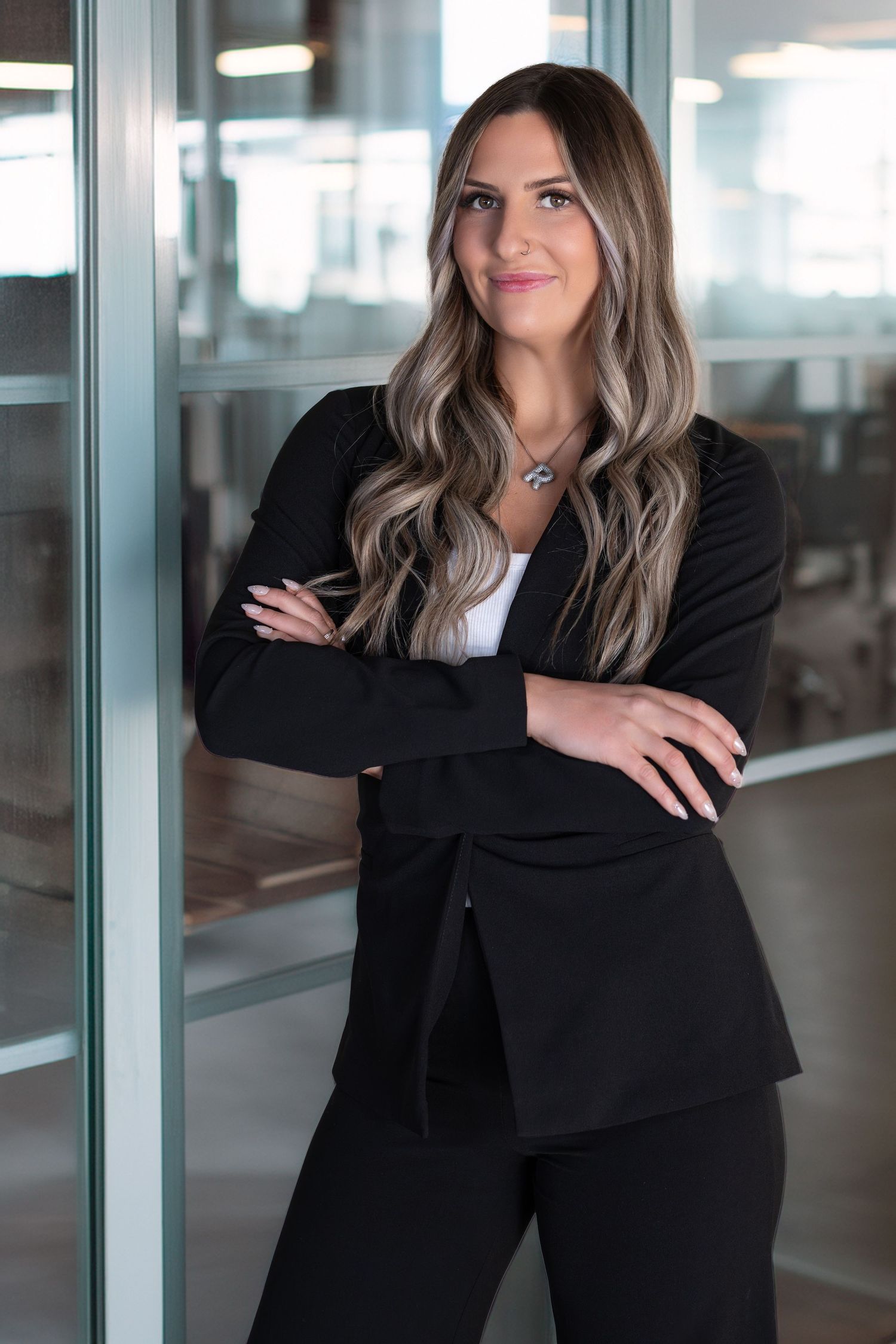 Professional woman in black blazer and pants stands confidently with arms crossed in a modern office setting.