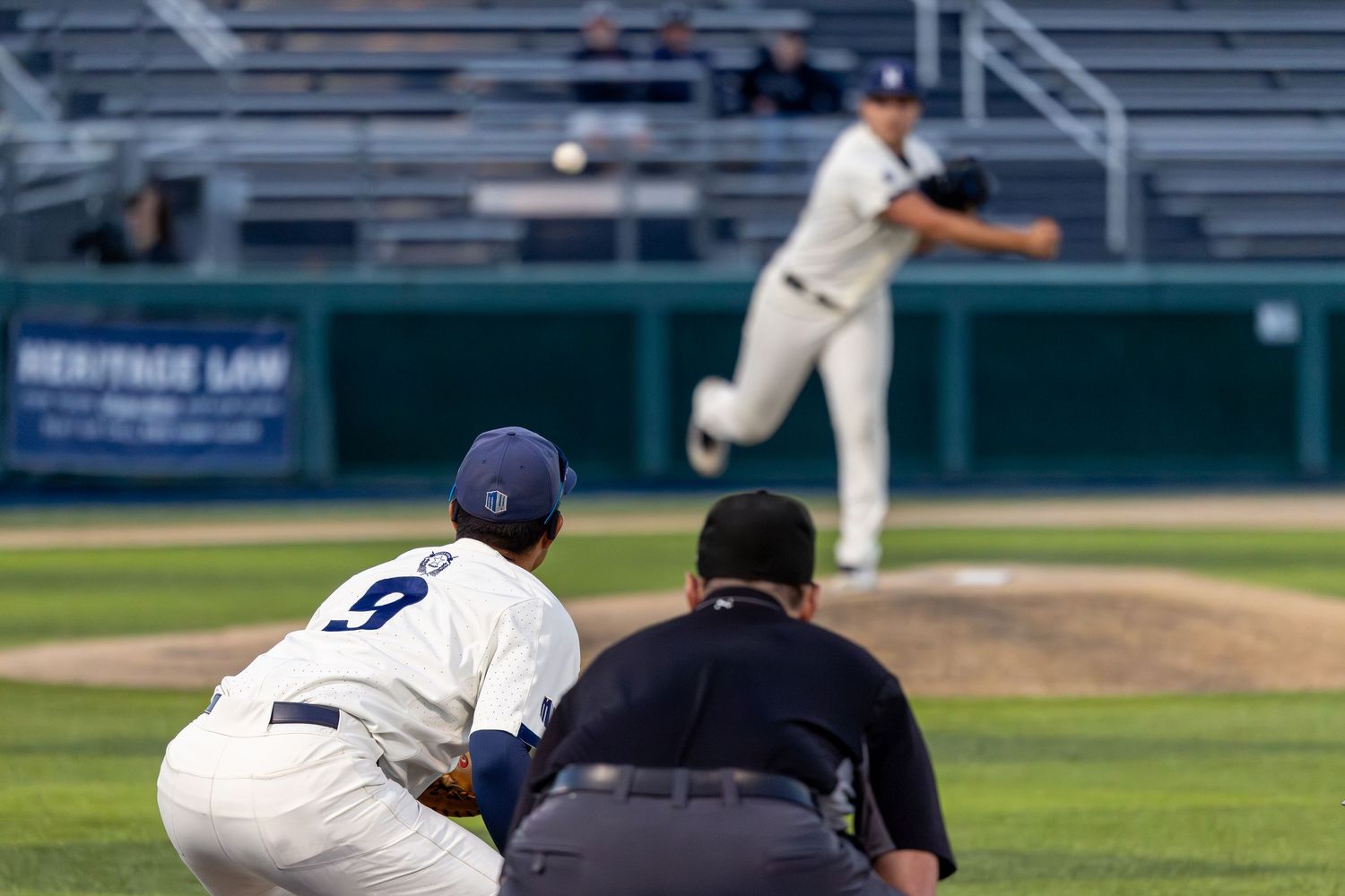 Baseball pitcher throwing a pitch during a game, with batter and umpire in the foreground at a professional stadium.