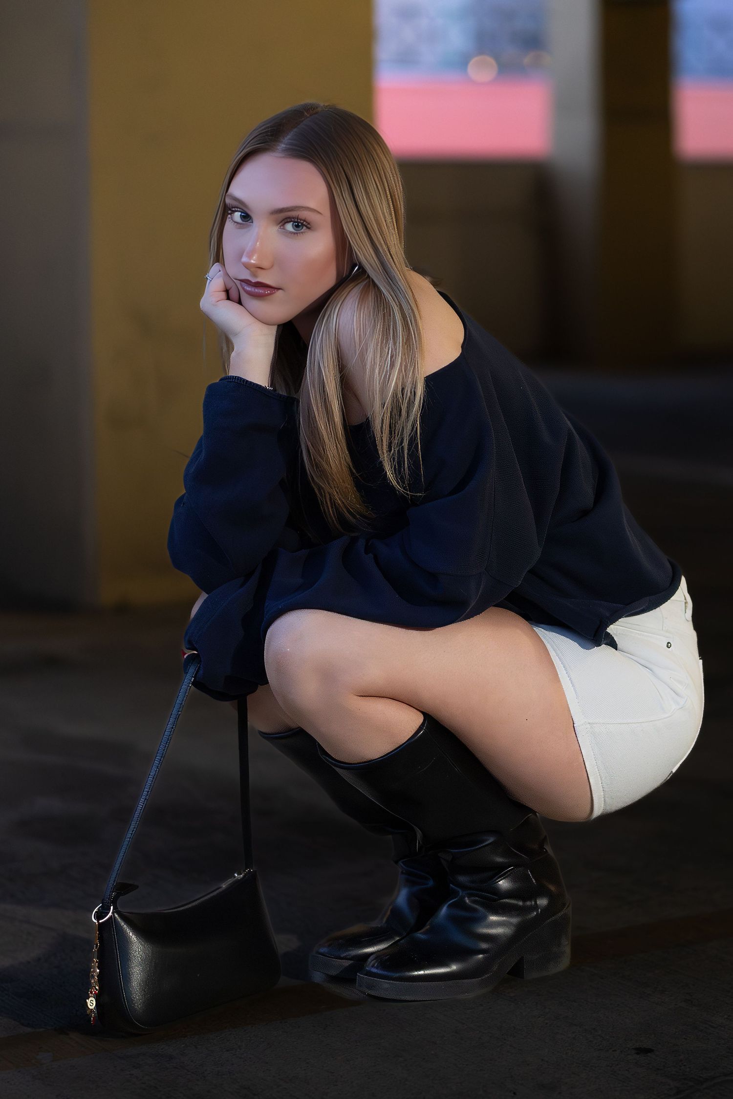 Fashion portrait of someone in a navy sweater and white shorts crouching in a dark urban setting with a small handbag.