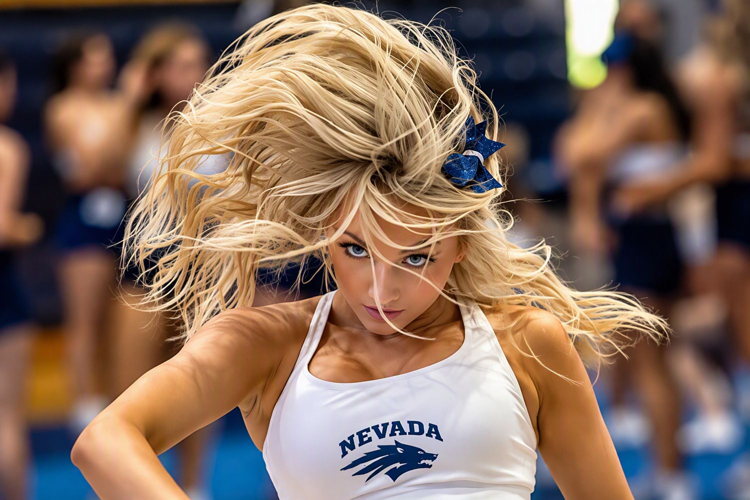 Cheerleader in a white Nevada tank top with a blue bow tosses her long blonde hair during a performance as teammates stand behind her.