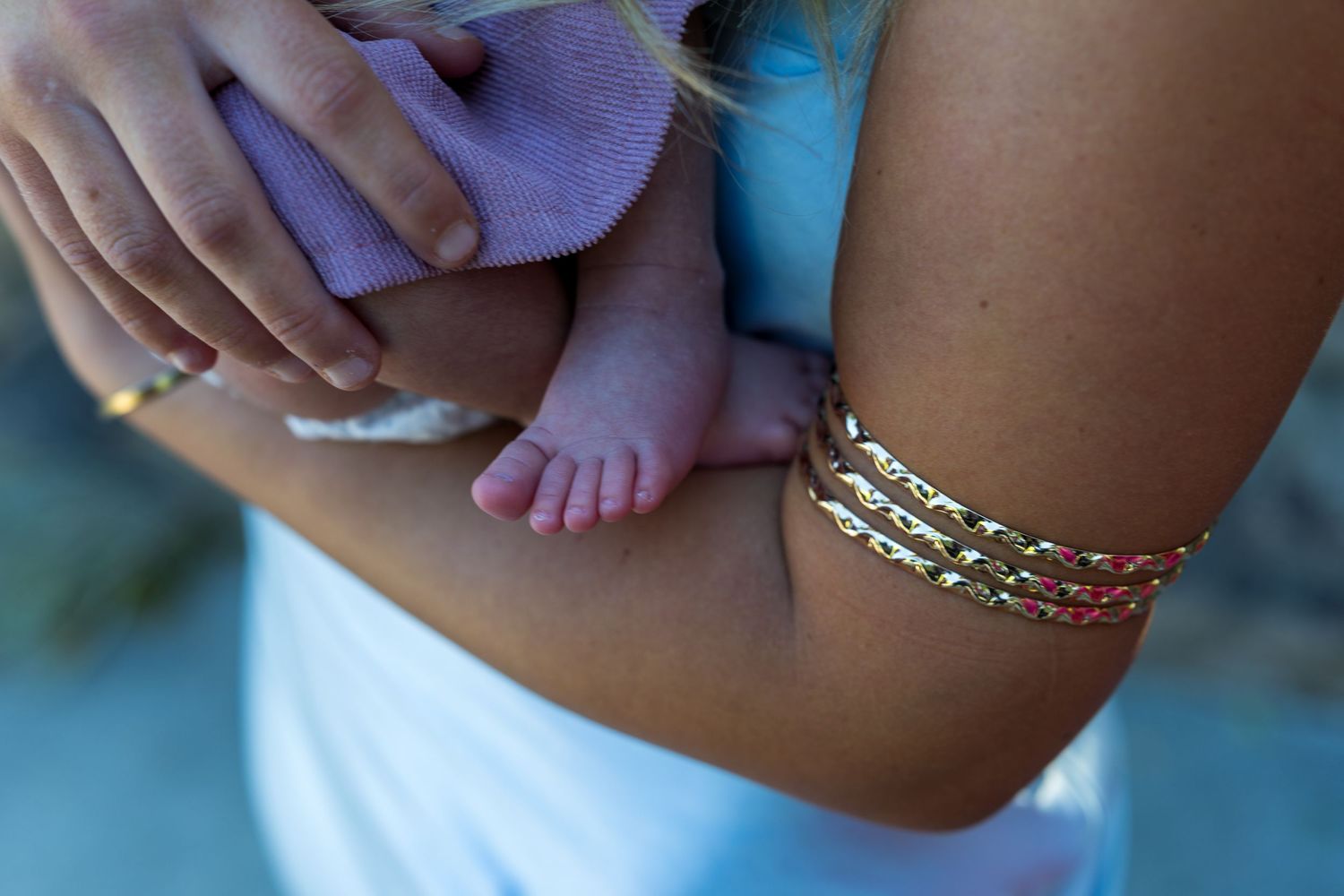 A tiny baby foot rests against an arm adorned with a delicate gold chain bracelet.