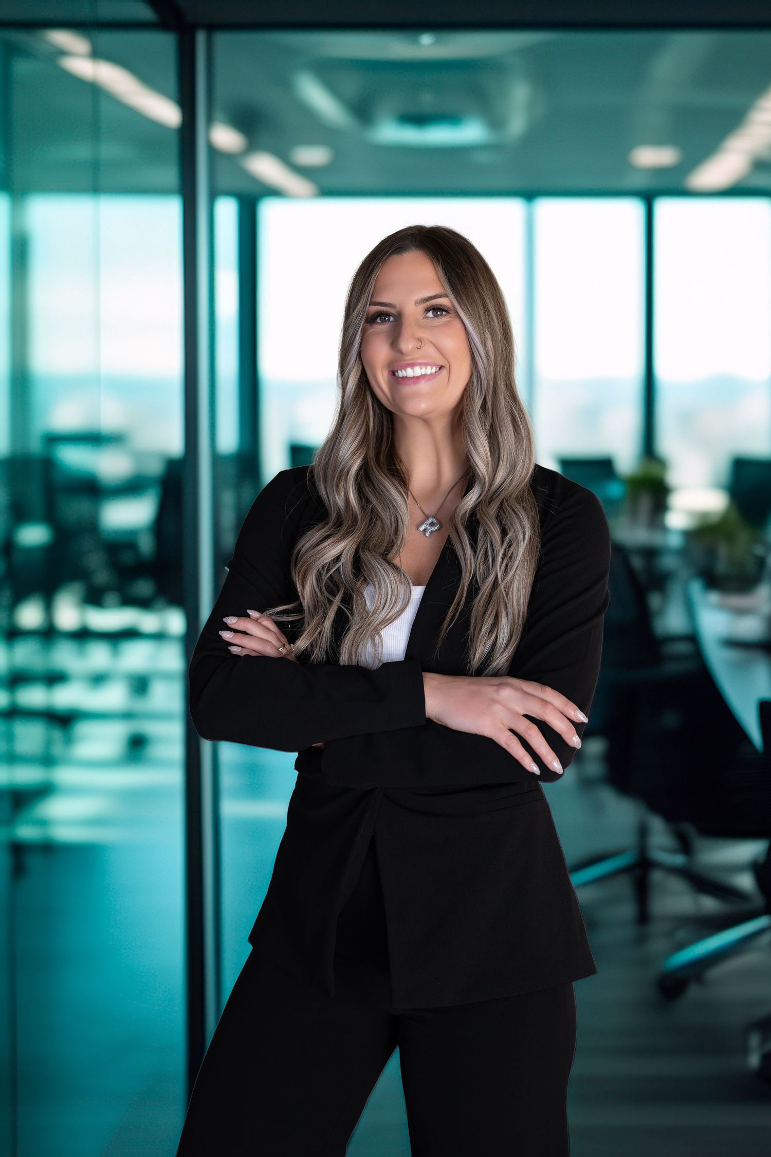 Professional businesswoman in black suit smiling with arms crossed in modern office.