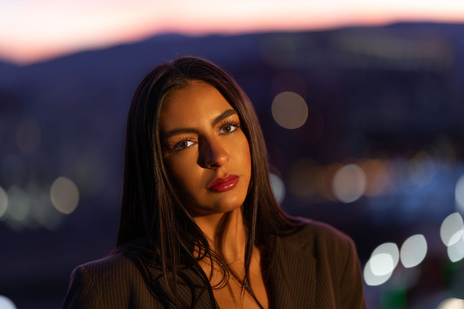 Portrait at twilight with city lights bokeh in background and warm evening lighting.