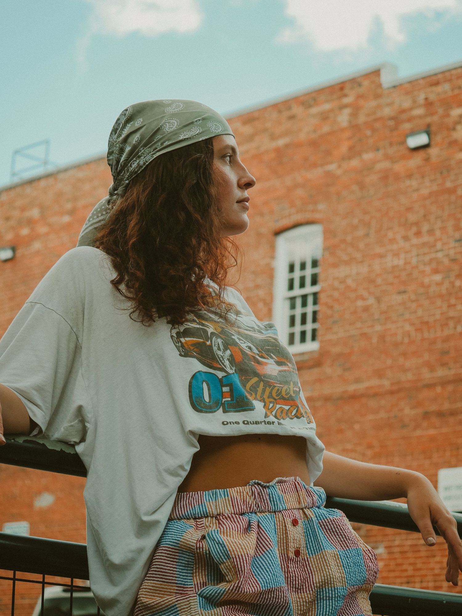 Stylish woman in denim and white t-shirt sitting on steps against brick wall background in warm lighting.