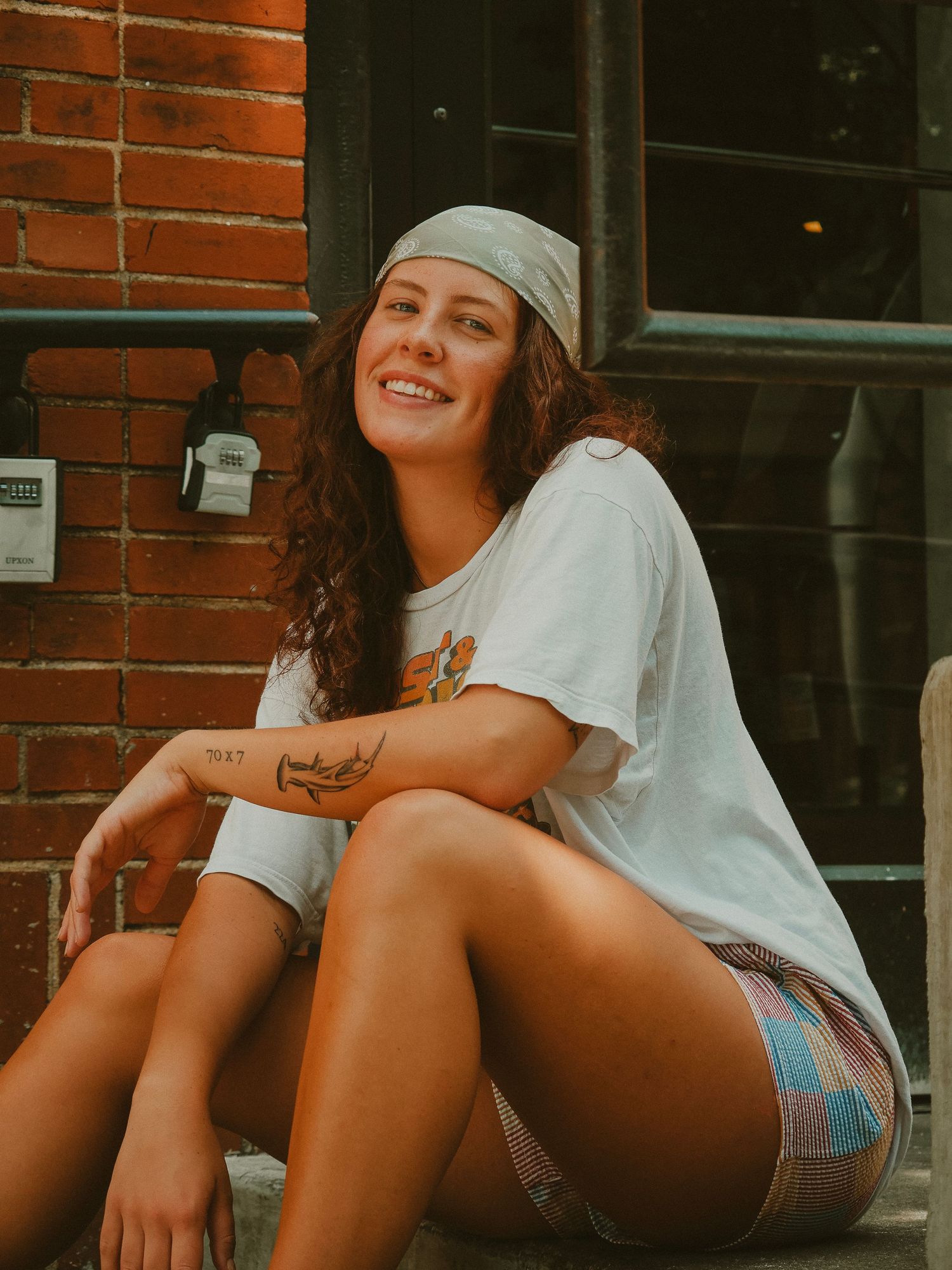 Three progressive shots of someone sitting casually against a brick wall wearing a white bandana and shorts in warm lighting.