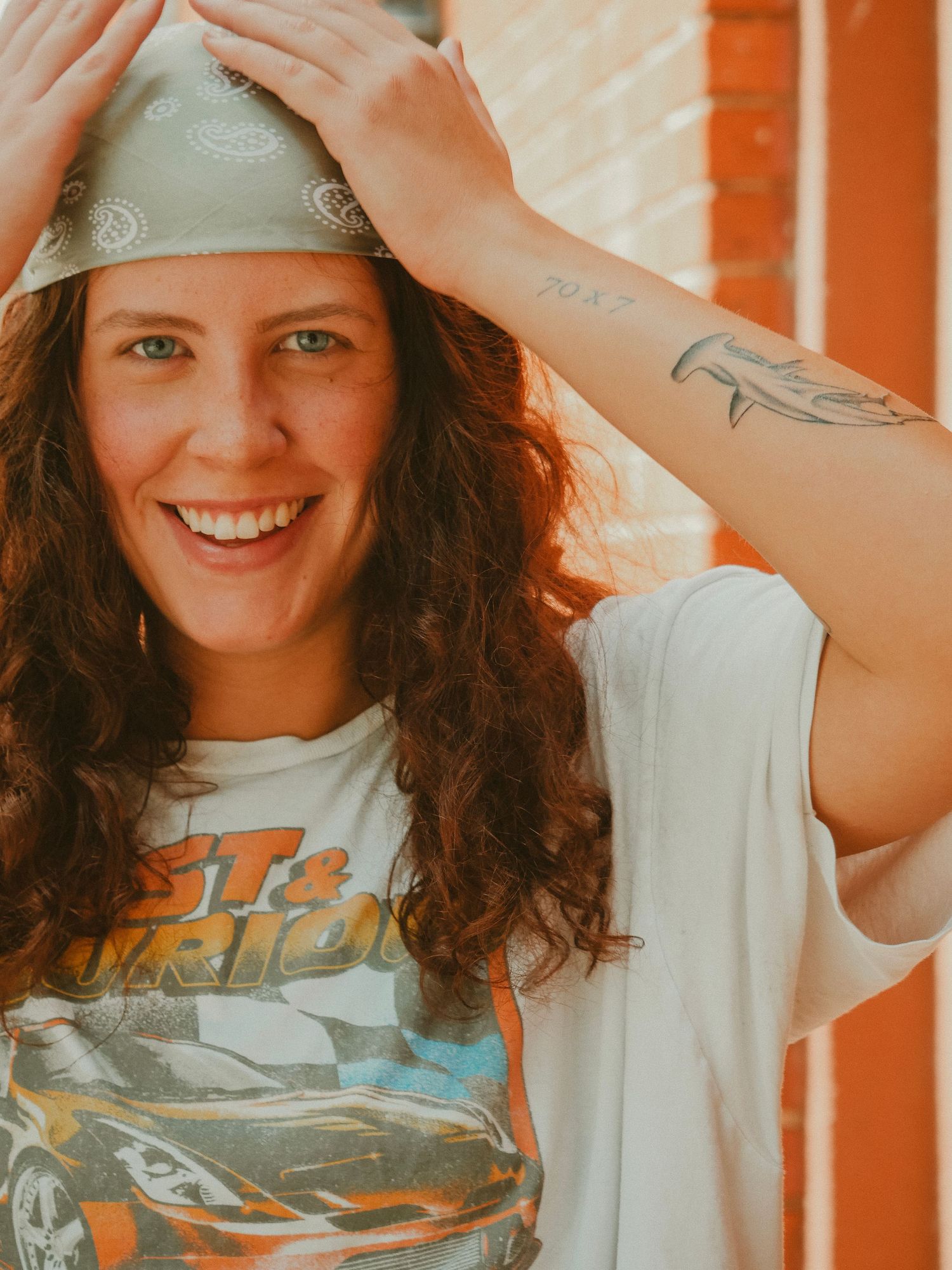 A person in a white t-shirt with curly hair poses playfully against an orange wall in a series of candid shots.