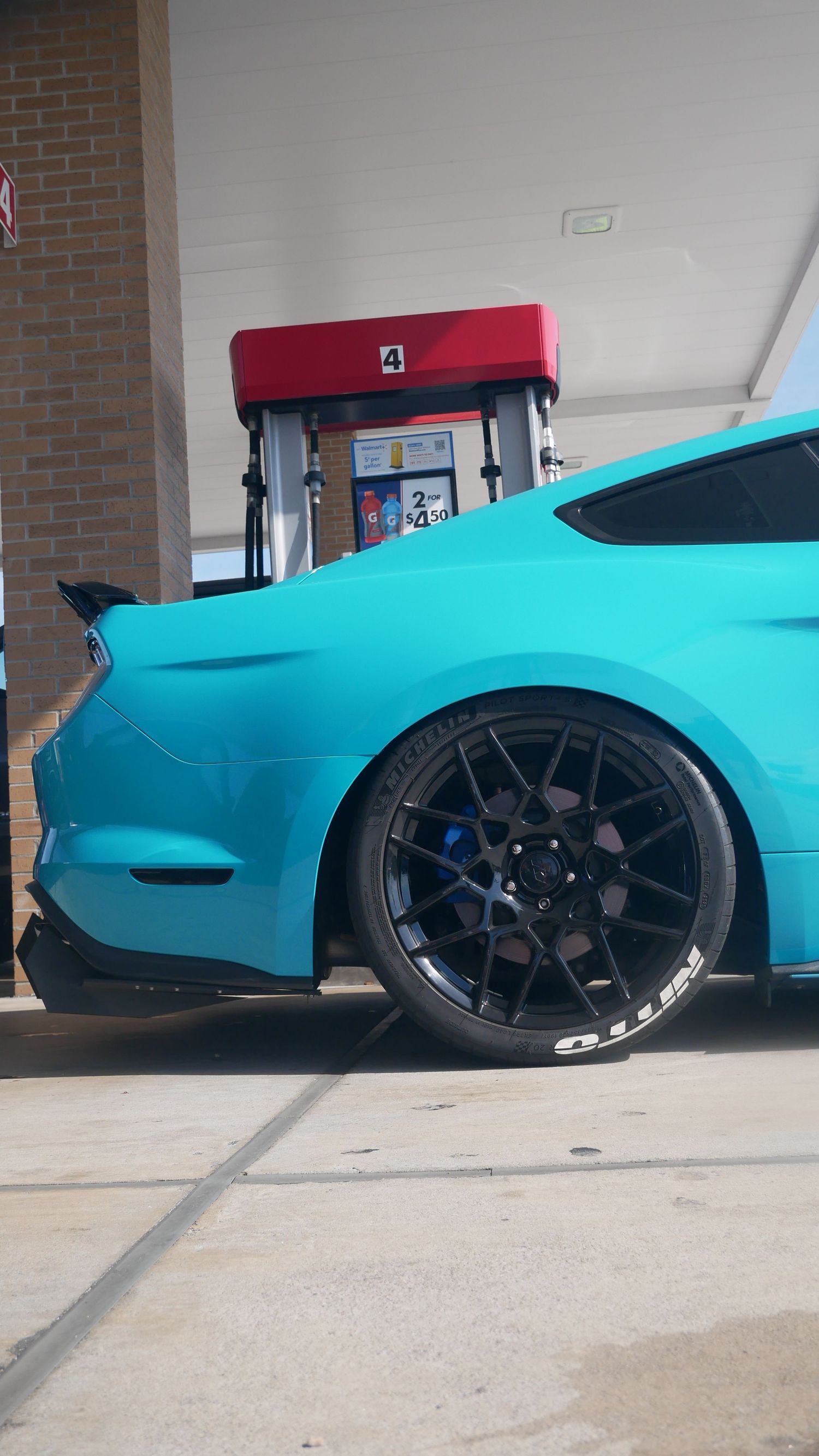 Turquoise Mustang with custom black wheels parked at a gas station.
