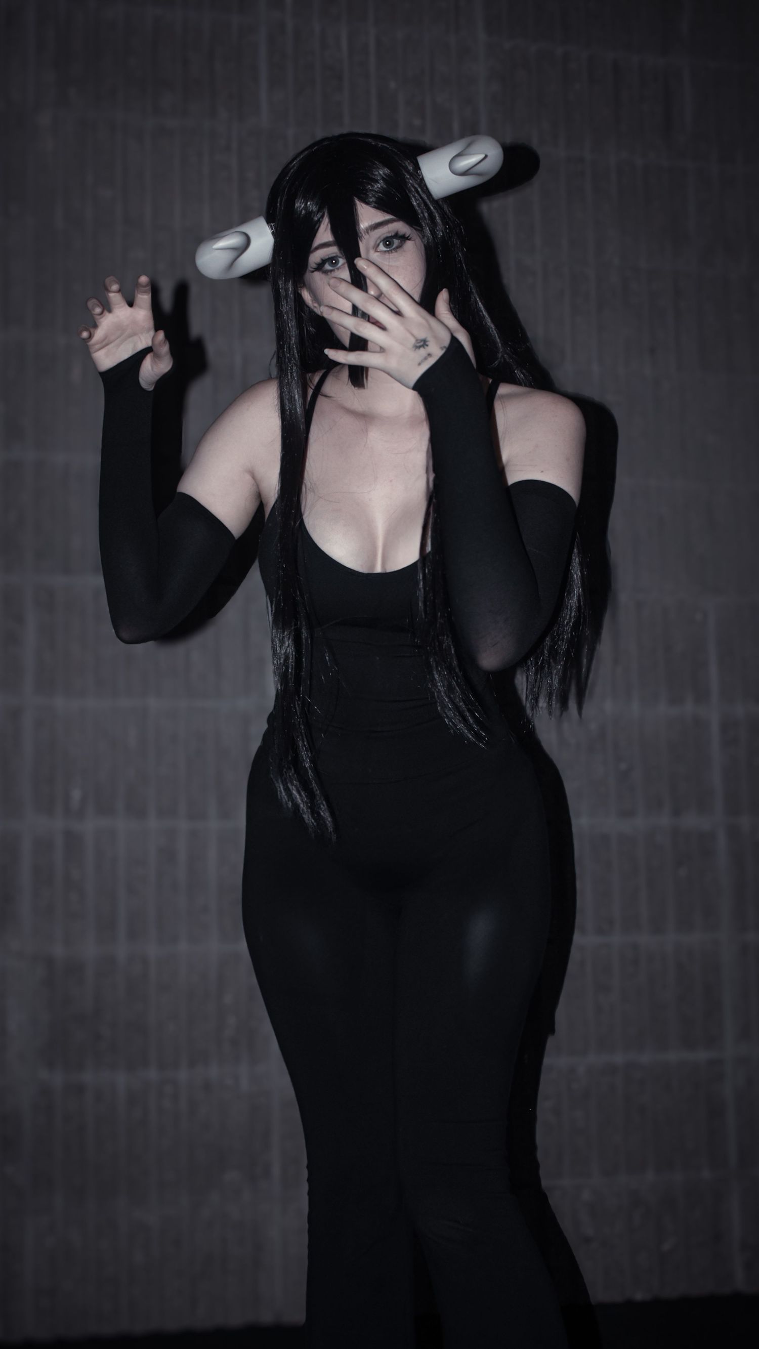 Moody cosplay photo featuring black bodysuit and white horned accessories against dark background.