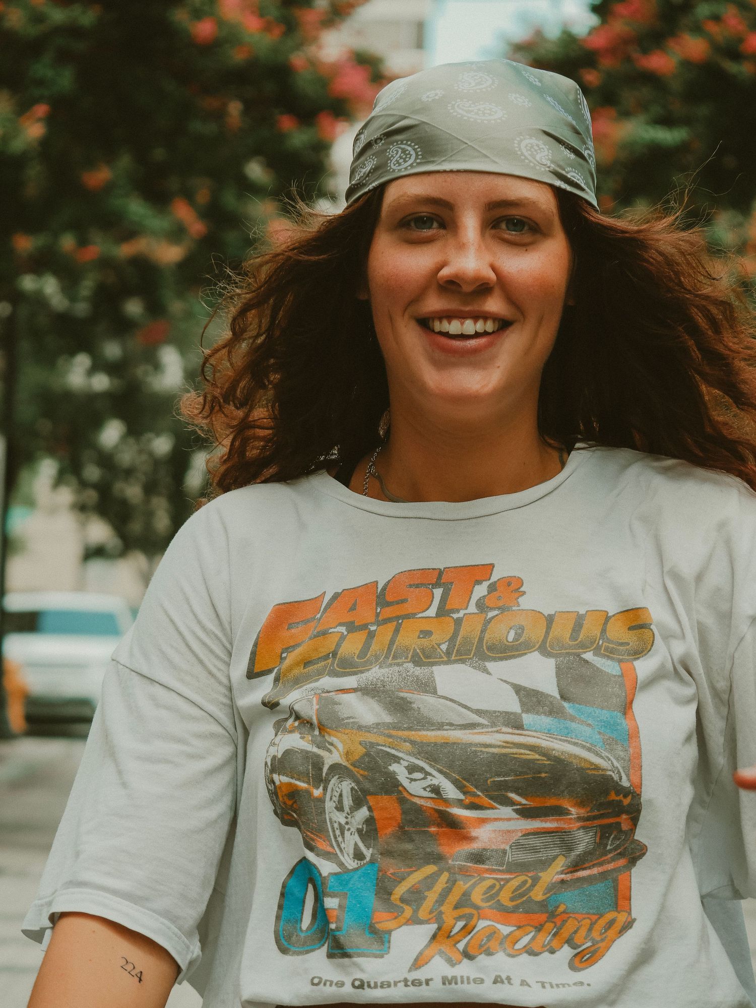 Person wearing a vintage Fast & Furious inspired t-shirt and gray beanie poses joyfully outdoors near autumn foliage.