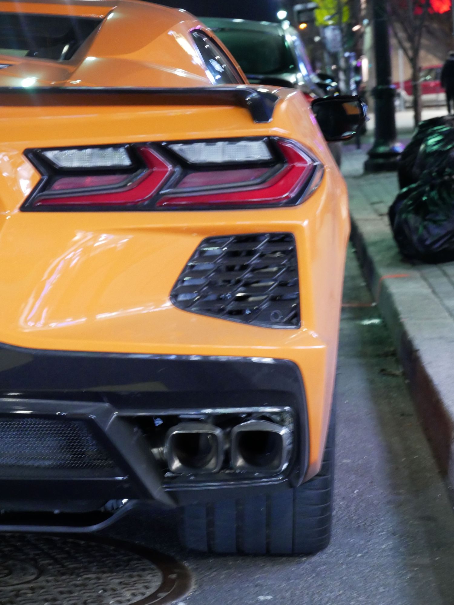 Rear corner detail of an orange Chevrolet Corvette C8 showing LED taillights and exhaust system.