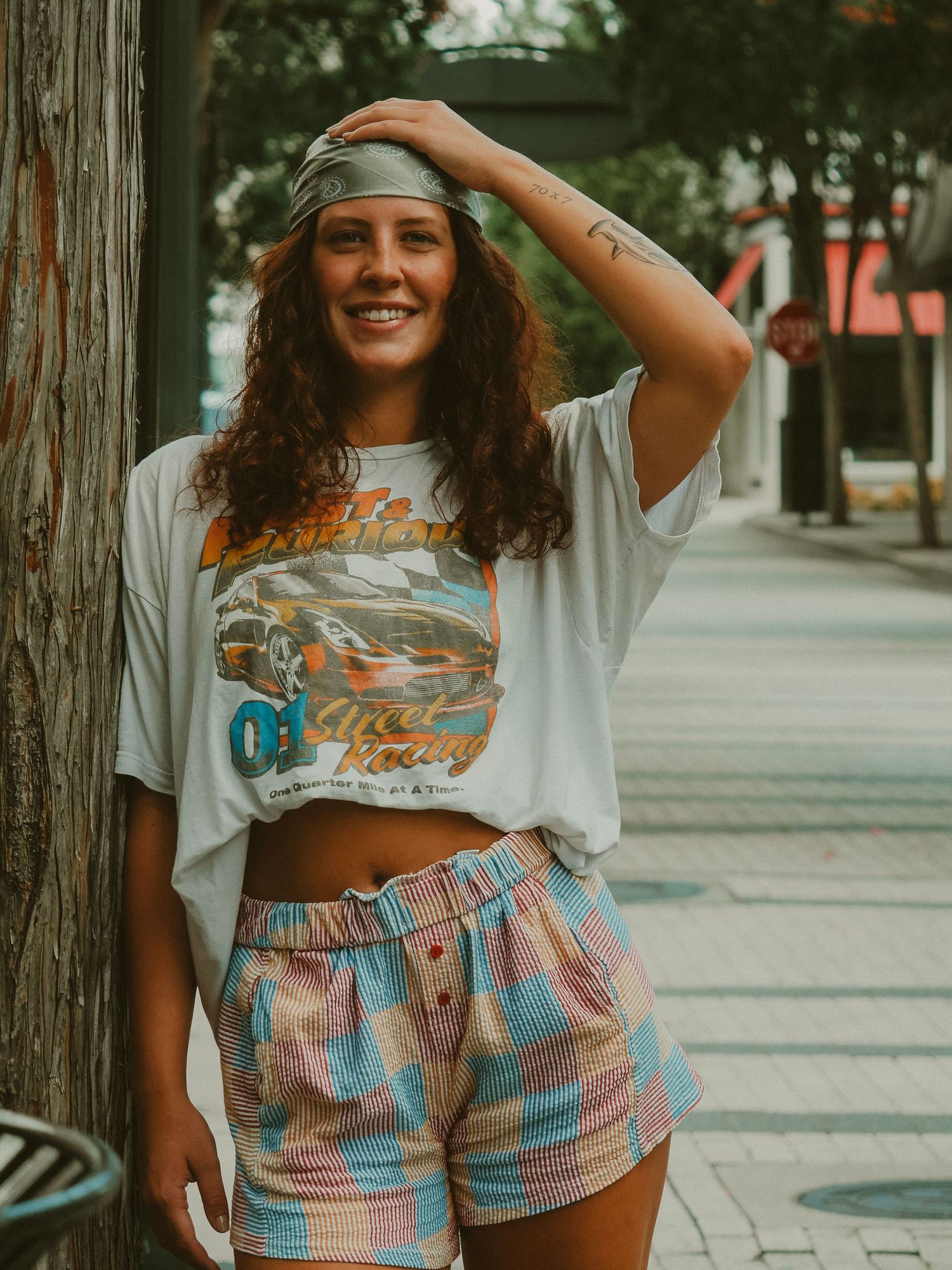Retro boho style outfit with cropped graphic tee, tie-dye shorts and headband on a city sidewalk in warm lighting.