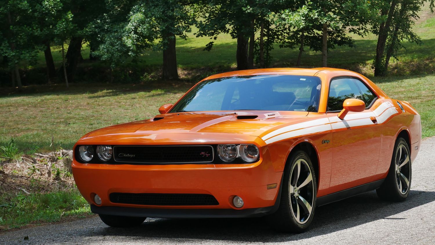 Modern orange Dodge Challenger showcasing its muscular design against green landscaping.