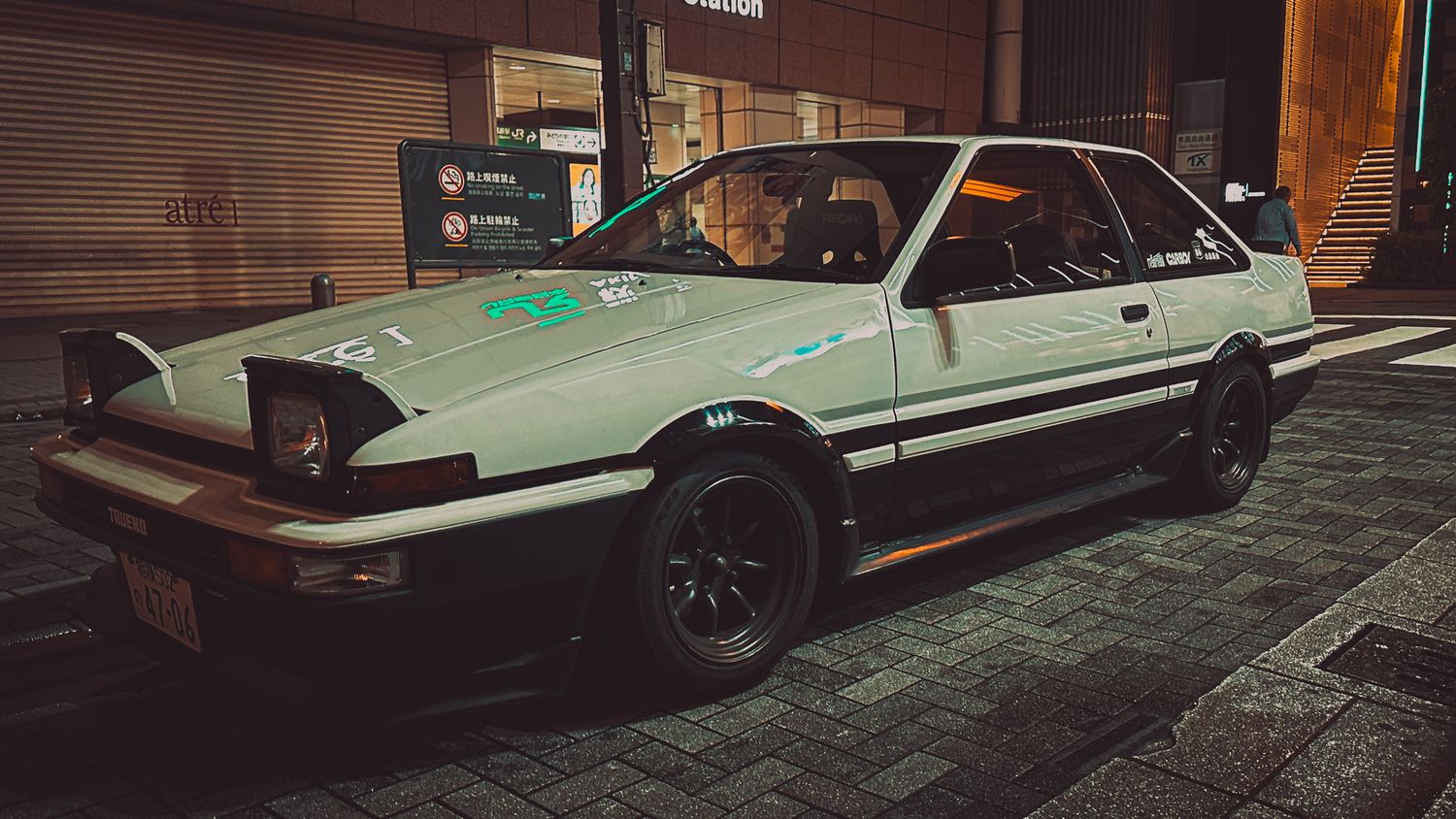 Classic Toyota Trueno AE86 sports car parked on a dark street with retro styling and black wheels.