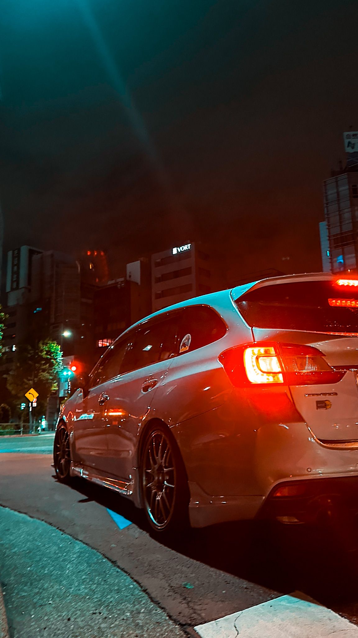 Modified sports car with glowing red taillights parked on a city street at night.