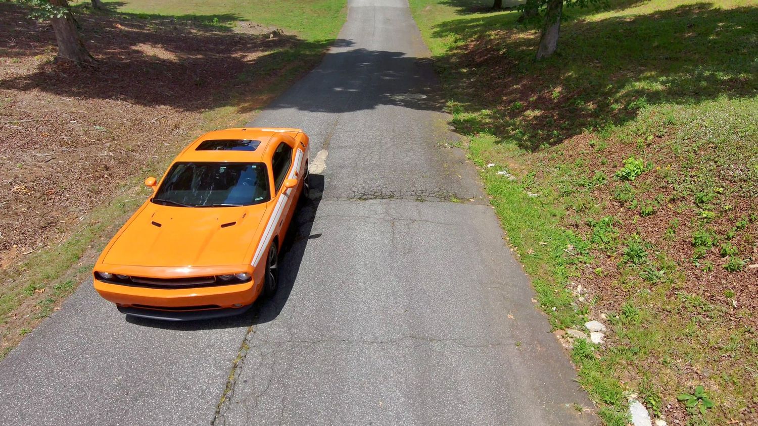 Wide angle shots of an orange muscle car positioned on a winding road through landscaped grounds.