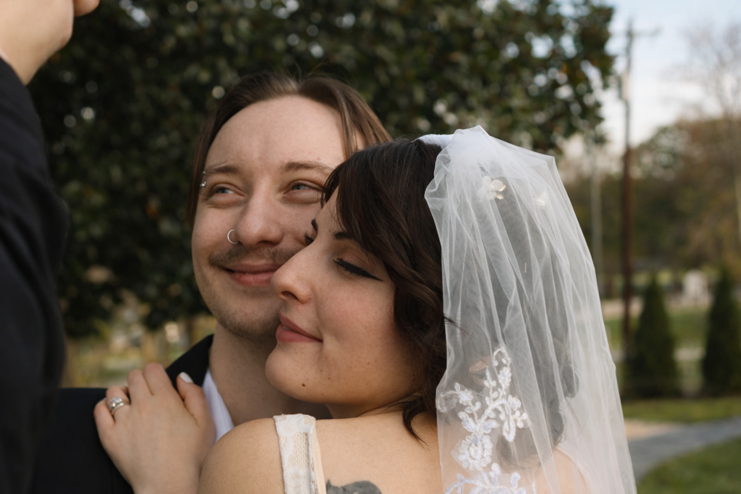 Couple in wedding attire embracing outdoors with lush greenery in the background.