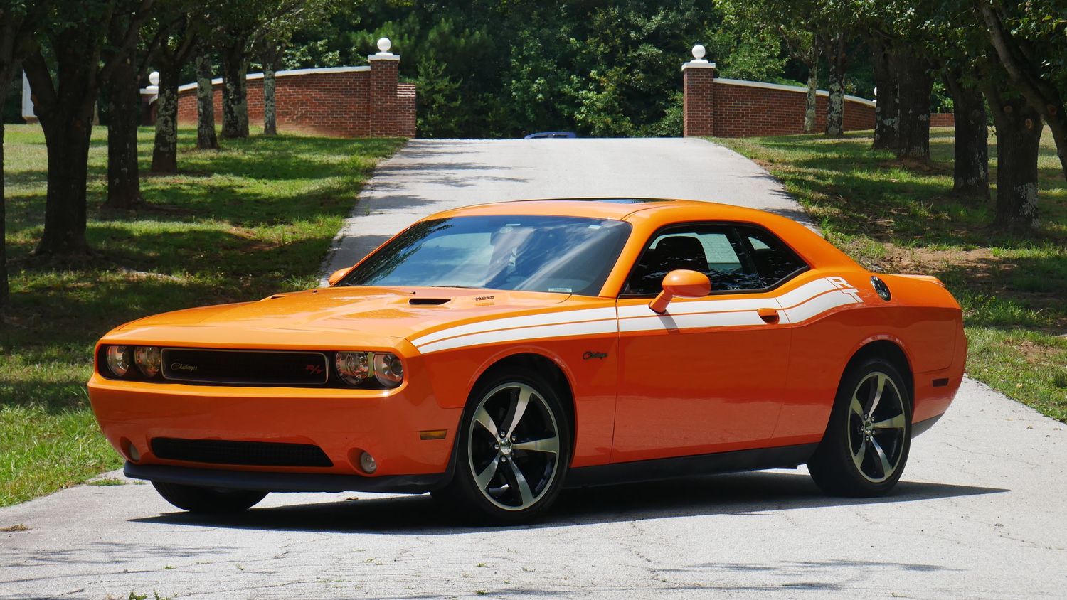 Orange Dodge Challenger with black five-spoke wheels on a tree-lined street.
