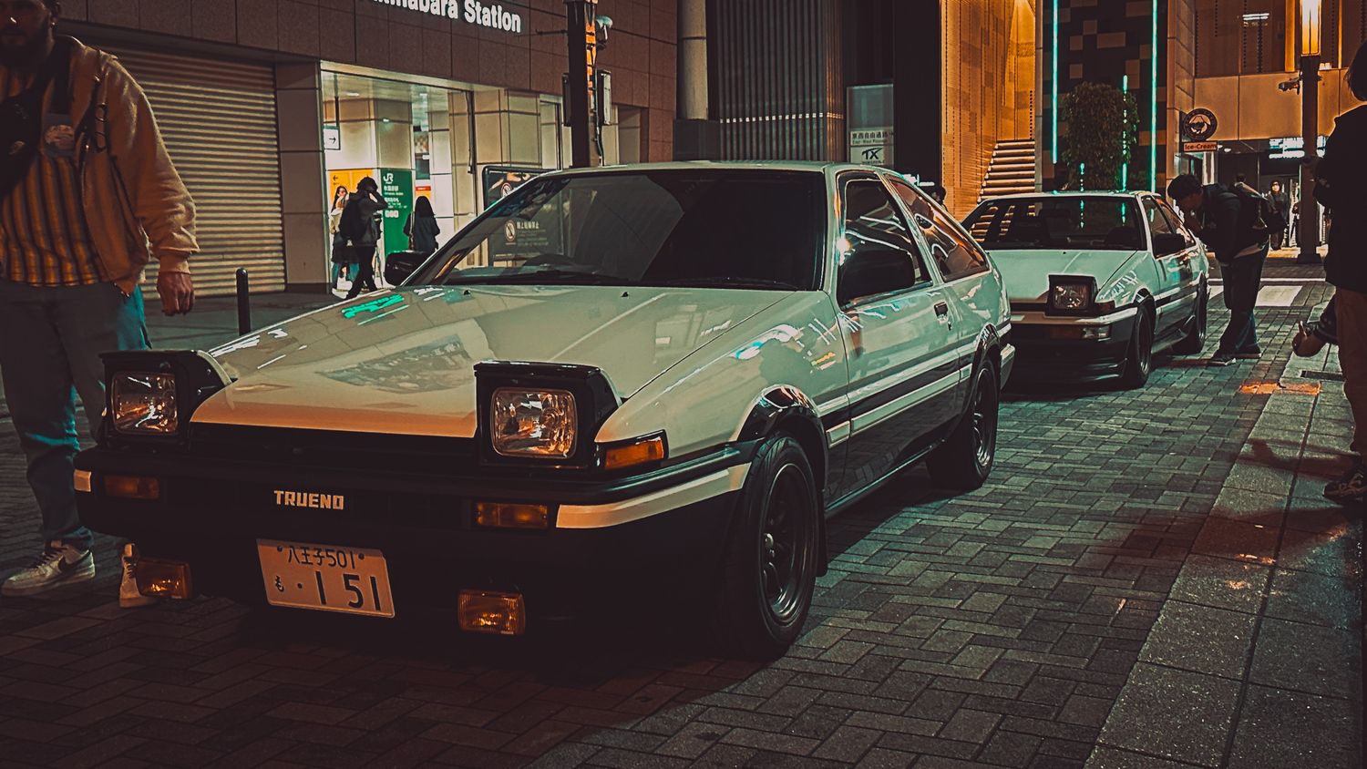 Classic sports cars parked along city street with warm ambient lighting.