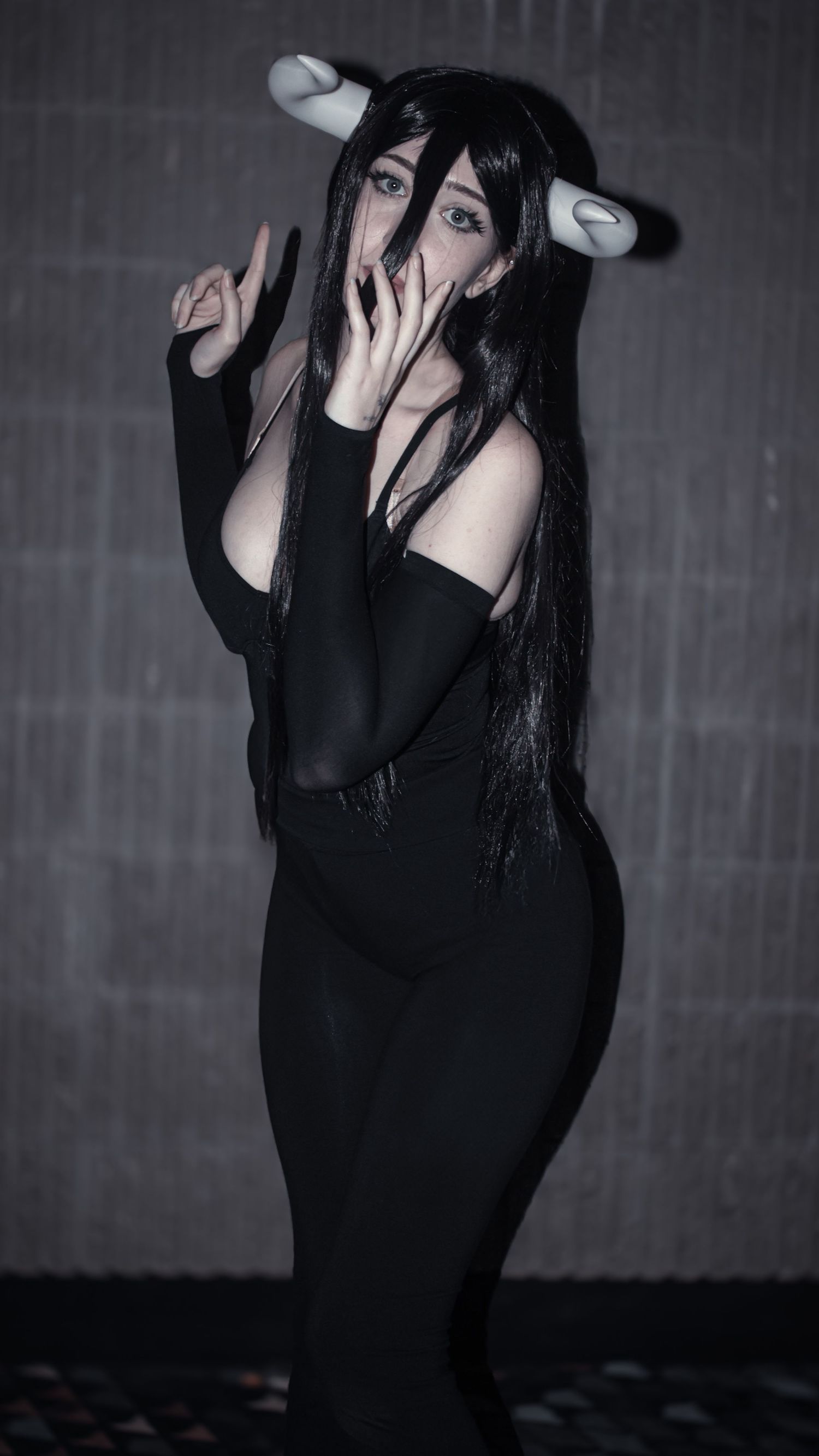 A figure in a black gothic outfit poses dramatically against a dark textured background.