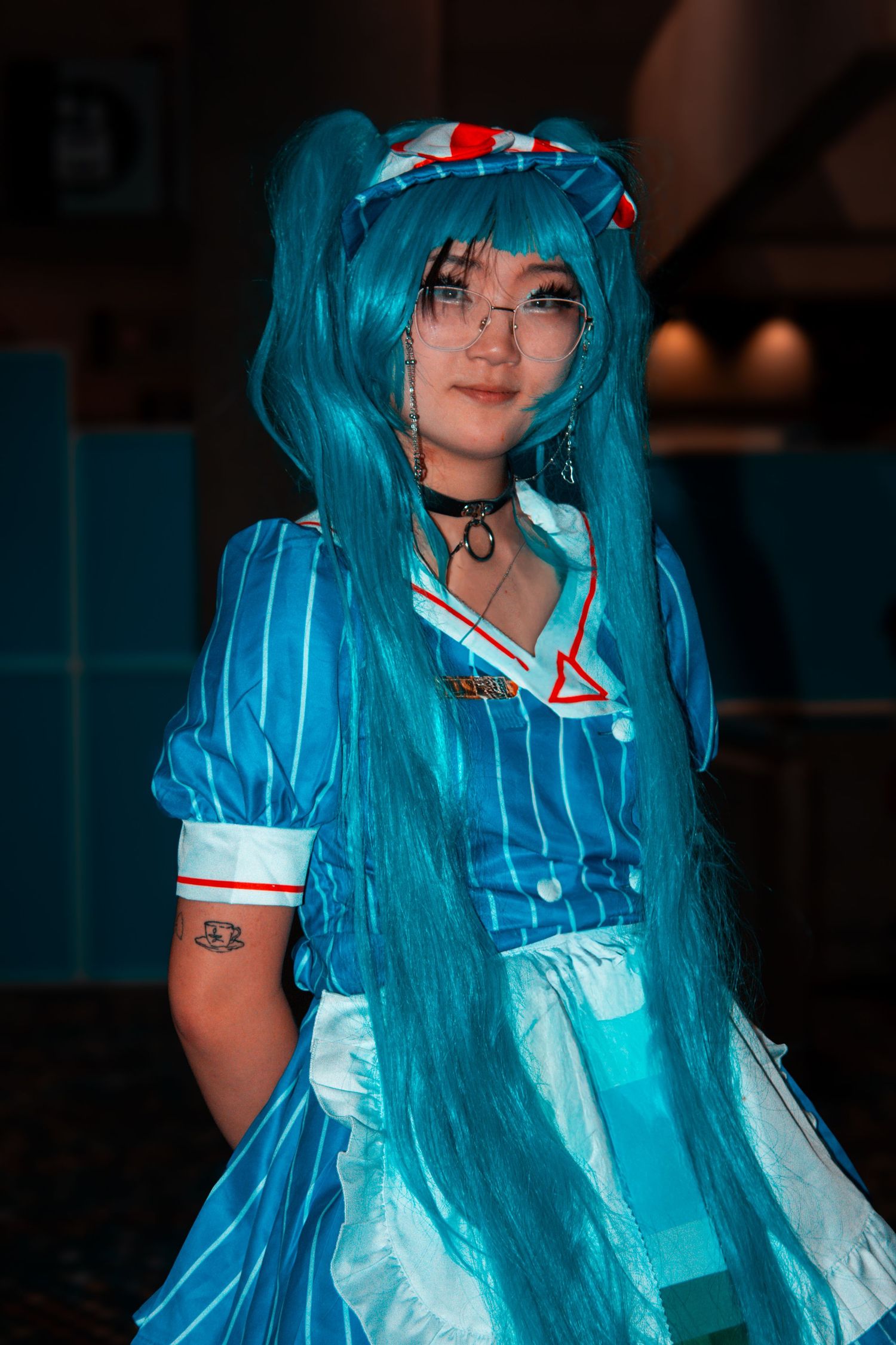 Cosplayer in turquoise wig wearing blue and white striped dress with accessories.
