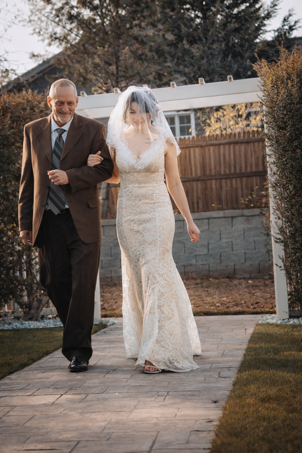 A couple walks down a stone path at an outdoor wedding ceremony on an autumn day.