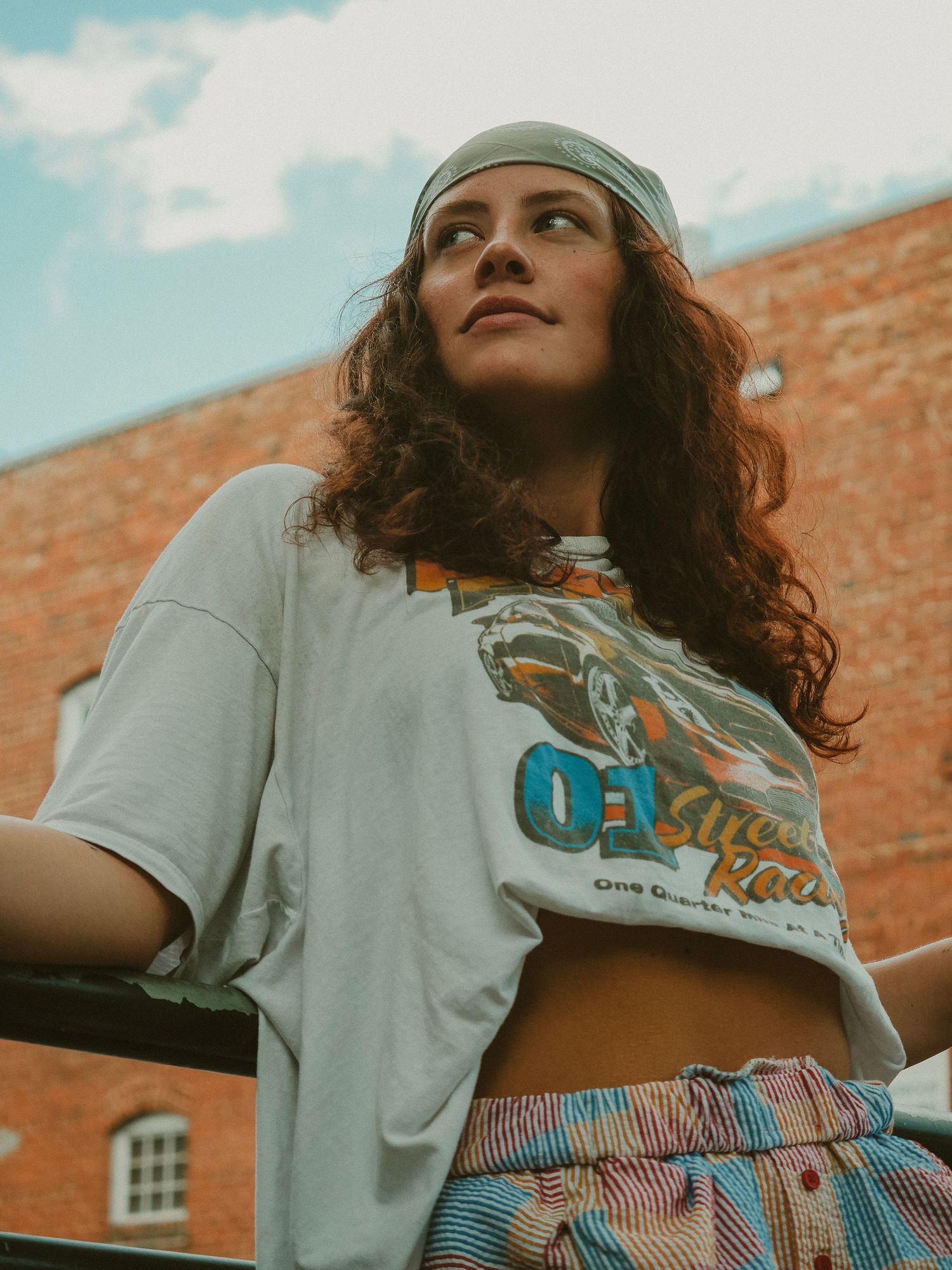 Fashion lifestyle shoot against brick wall with model in striped skirt and graphic tee showing casual summer style.