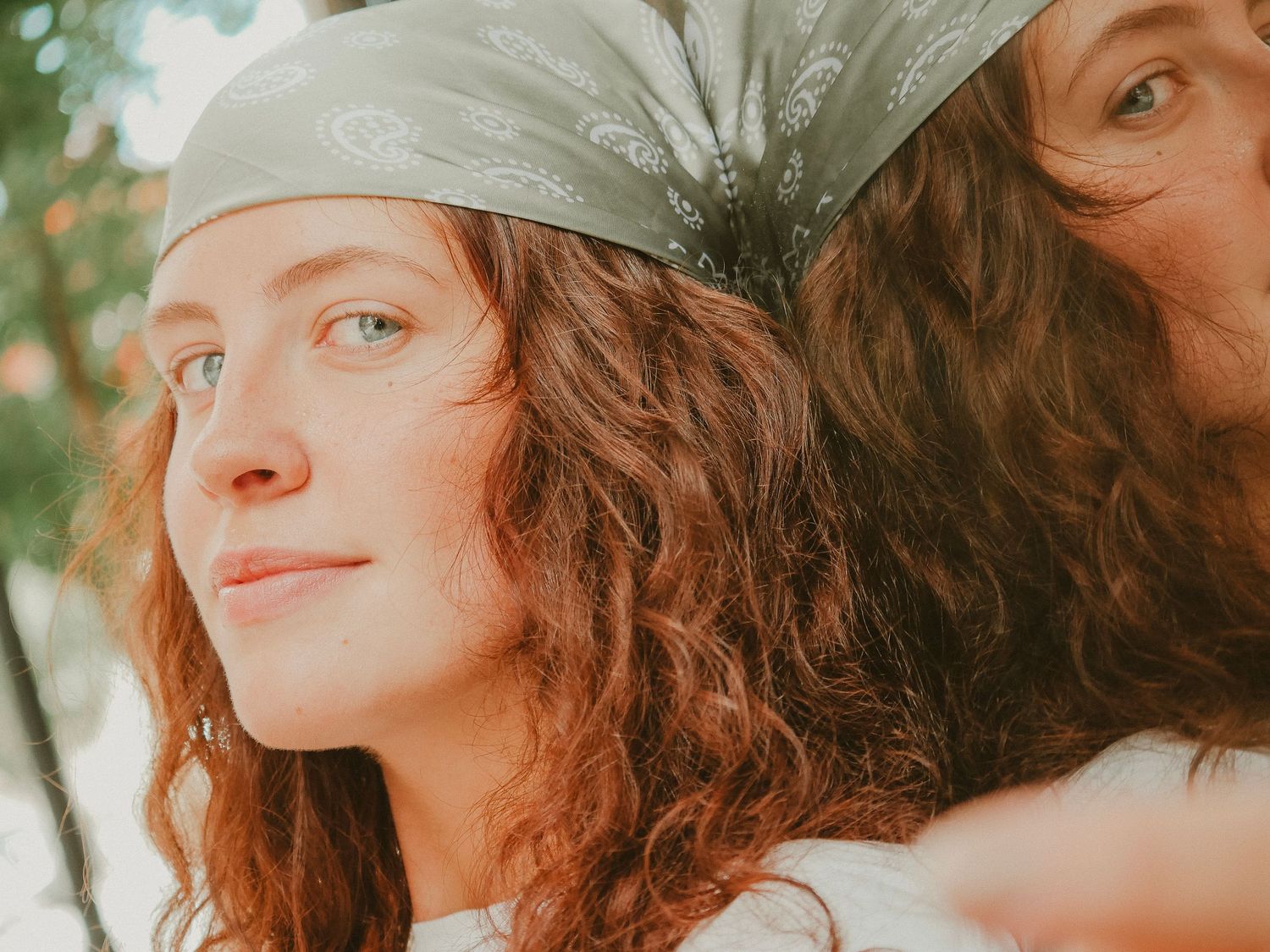 Close-up portrait of someone with curly red hair wearing a sage green headscarf looking off to the side with dreamy expression.
